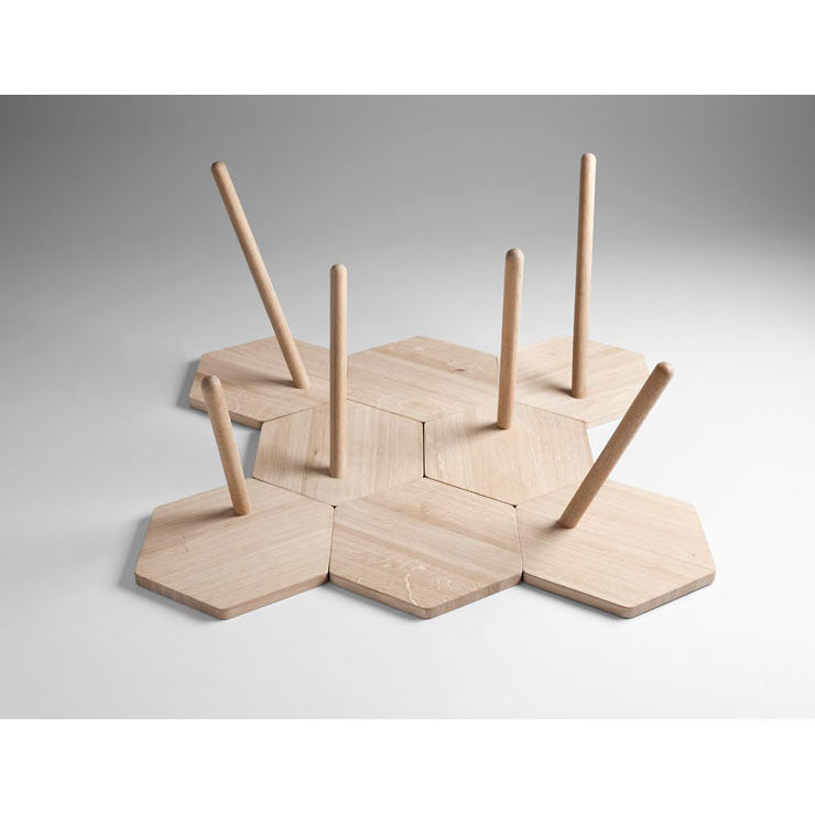 Lean Tables by Coordination Berlin are composed of interconnected wooden hexagonal oak pieces, each featuring a central vertical rod. This contemporary design creates a striking geometric pattern with its contrasting light wood against a plain background.