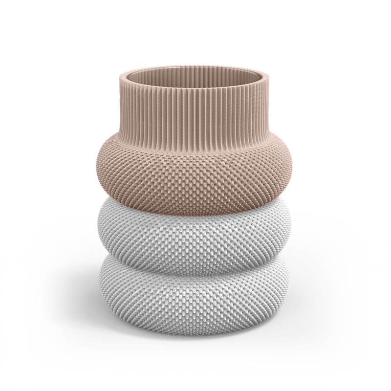 The Dorn 110g Vase by Sheyn is a modern, eco-friendly creation made through 3D printing. It features a wide cylindrical top in soft pink, a textured gray middle section, and a glossy white base, resembling stacked, textured rings.