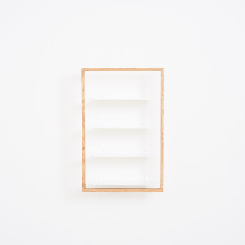 The Basti - Presentation by Das kleine b is a minimalist wooden frame shelf featuring four white tiers, ideal as a contemporary shoe rack. Mounted on a plain white wall, its modern design highlights clean lines, providing an uncluttered and adaptable solution for any space.