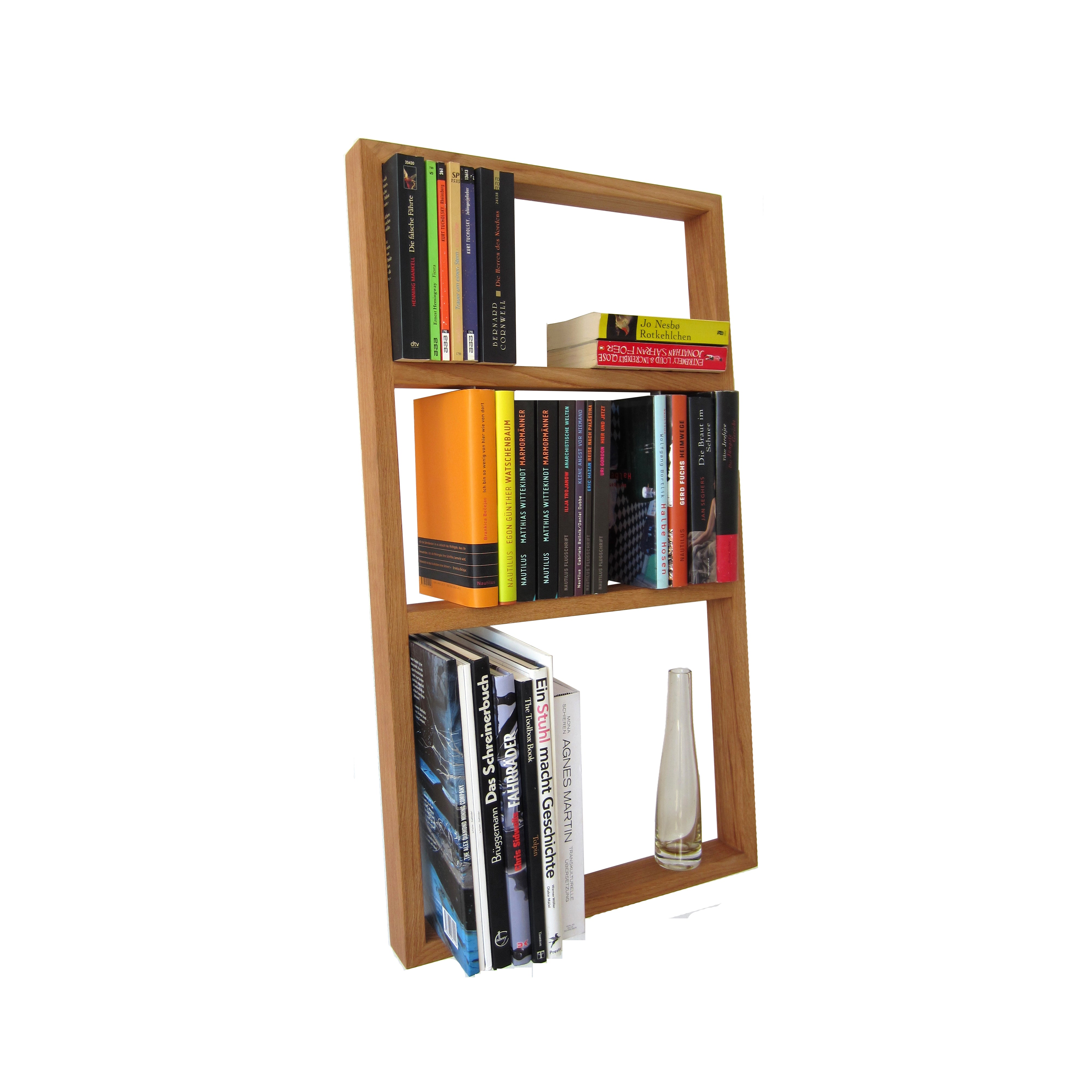 The Bertold by Das kleine b is an oak and stainless steel bookshelf featuring three unevenly spaced sections. Two sections hold upright and stacked, colorful books of standard height, while a slender glass vase sits below, creating a stylish display against a pristine white background.
