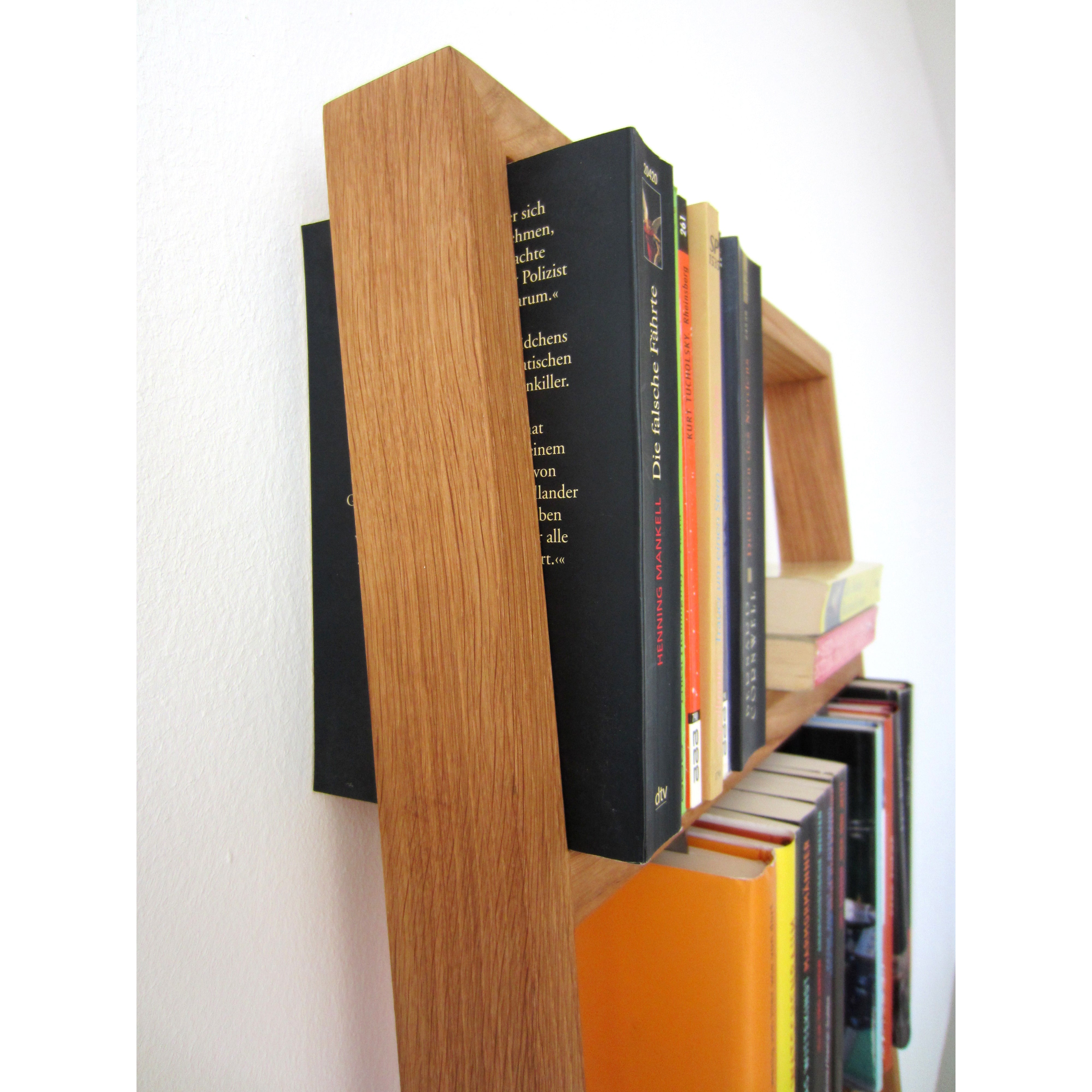 Close-up of Das kleine bs Bertold floating oak and stainless steel bookshelf on a white wall, featuring books with colorful spines. Its simple, modern design beautifully showcases the natural wood grain.