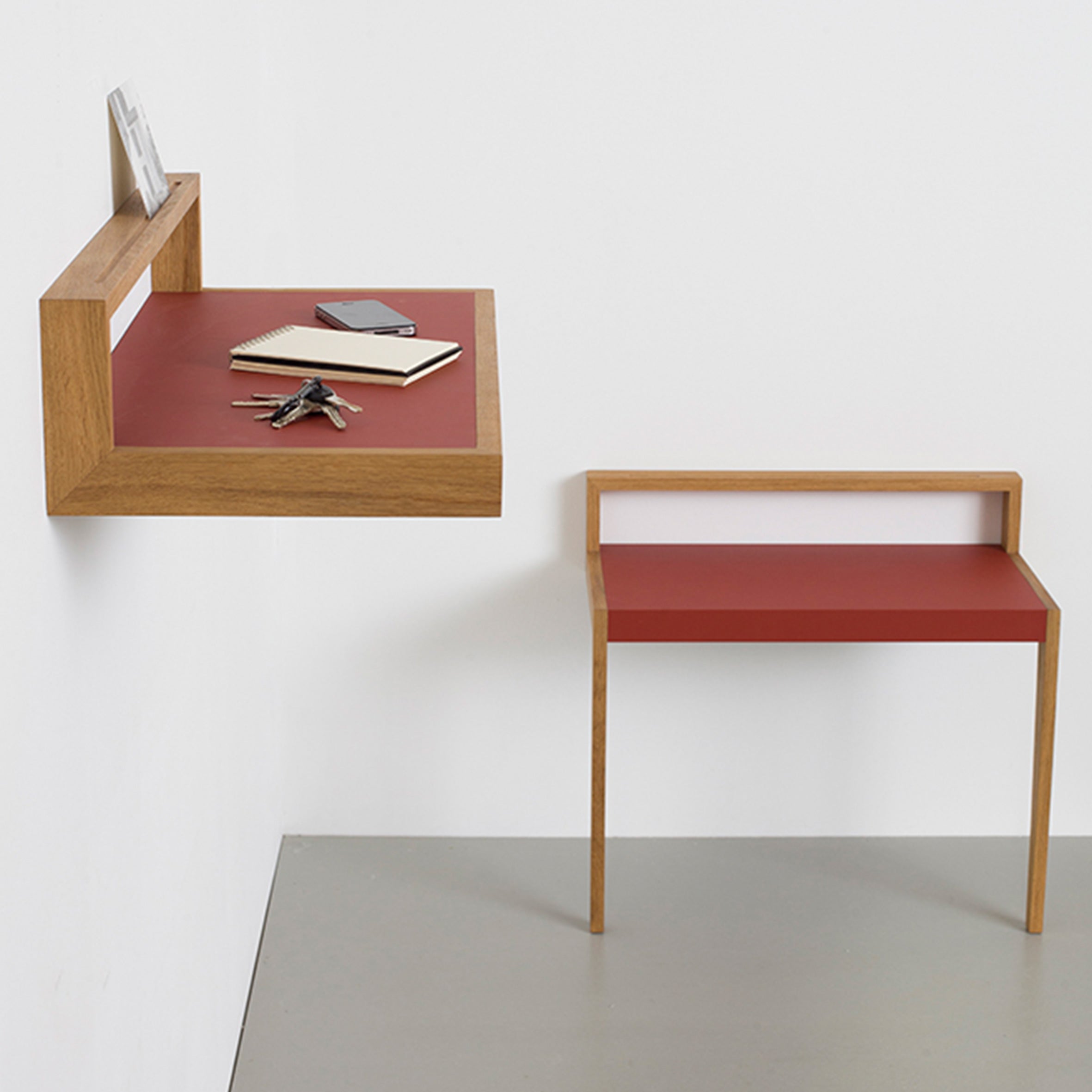 The Buck by Das kleine b is a minimalist wooden desk and wall-mounted storage shelf with a vibrant red linoleum surface. The cohesive design features an adaptable furniture style, matching units, and includes space for a small notebook, pen, and keys.
