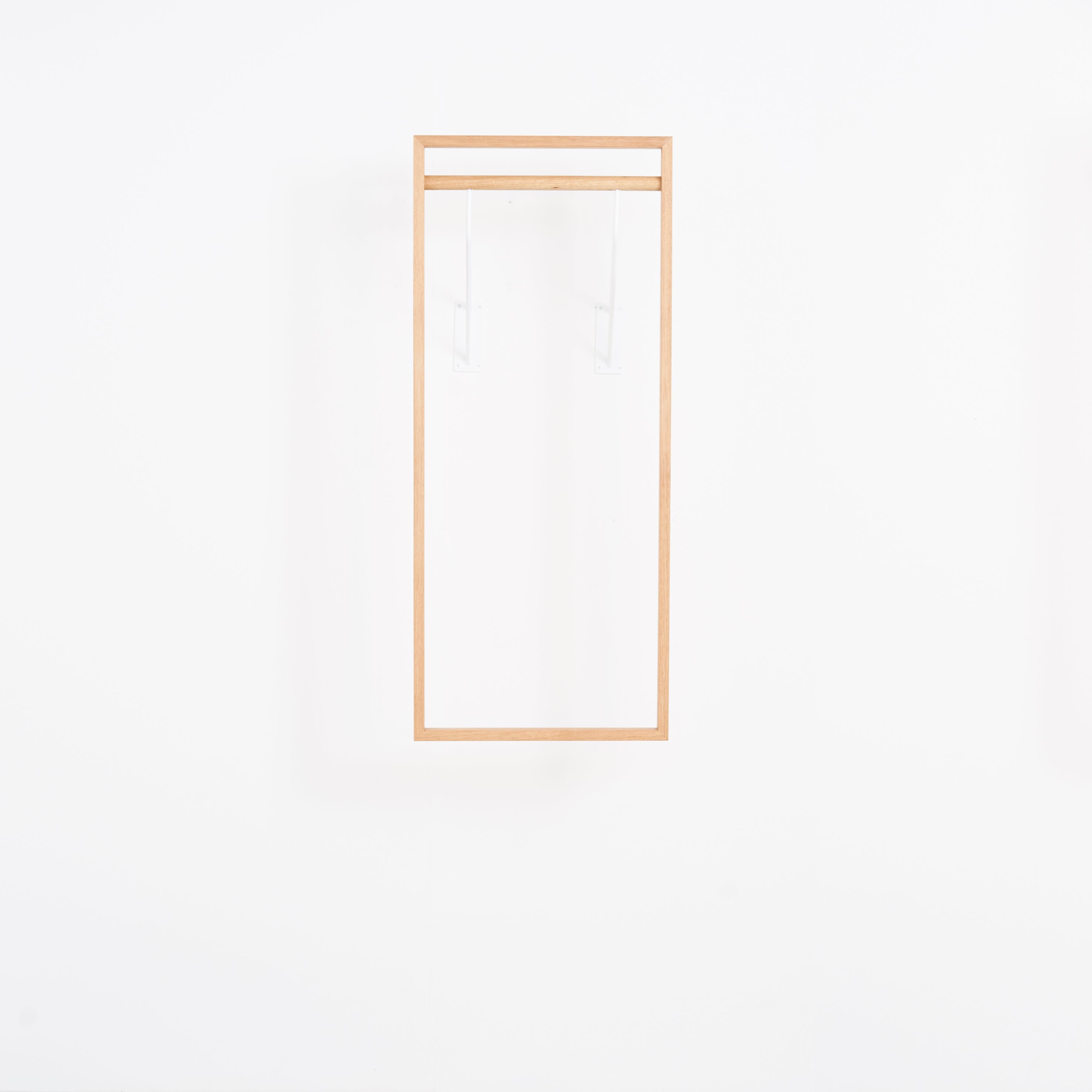 The Gardero-b by Das kleine b is a minimalist, rectangular wooden frame that resembles a hall stand with clean lines. It appears to float on a white wall with transparent supports, creating an illusion of expanded wardrobe space while emphasizing simplicity and elegance.