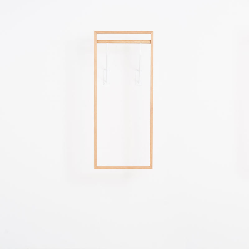 The Gardero-b by Das kleine b is a minimalist, rectangular wooden frame that resembles a hall stand with clean lines. It appears to float on a white wall with transparent supports, creating an illusion of expanded wardrobe space while emphasizing simplicity and elegance.