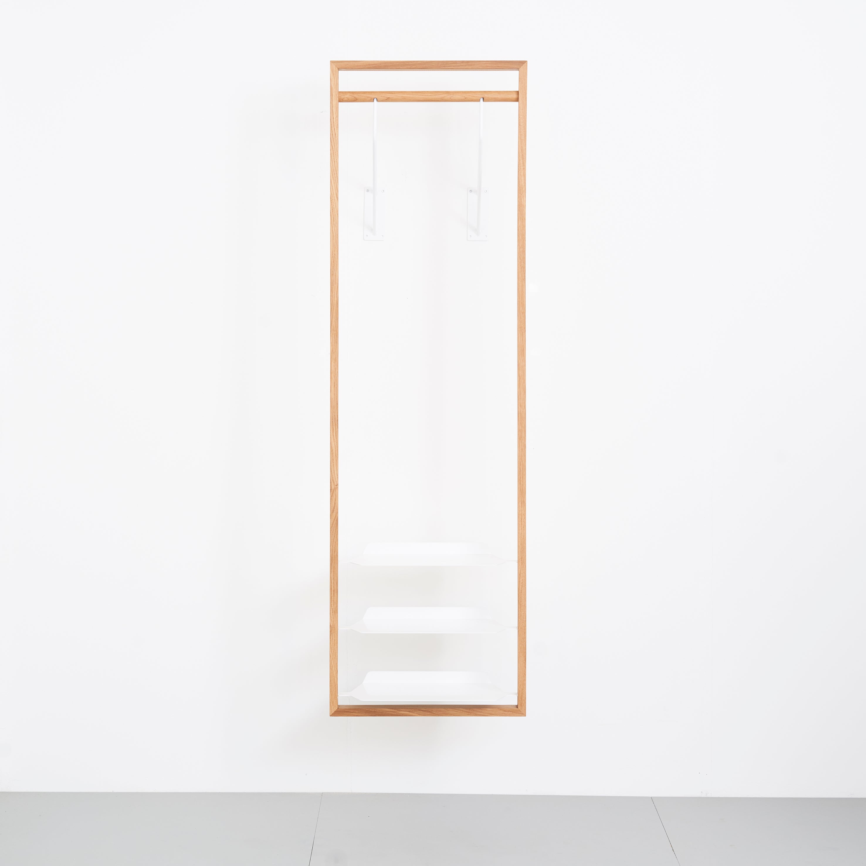 The Gardero-b by Das kleine b is a minimalist wooden frame mounted on a white wall, featuring three clear shelves and two transparent hanging rods, designed as a modern hall stand for displaying shoes or optimizing wardrobe space.