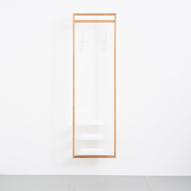 The Gardero-b by Das kleine b is a minimalist wooden frame mounted on a white wall, featuring three clear shelves and two transparent hanging rods, designed as a modern hall stand for displaying shoes or optimizing wardrobe space.