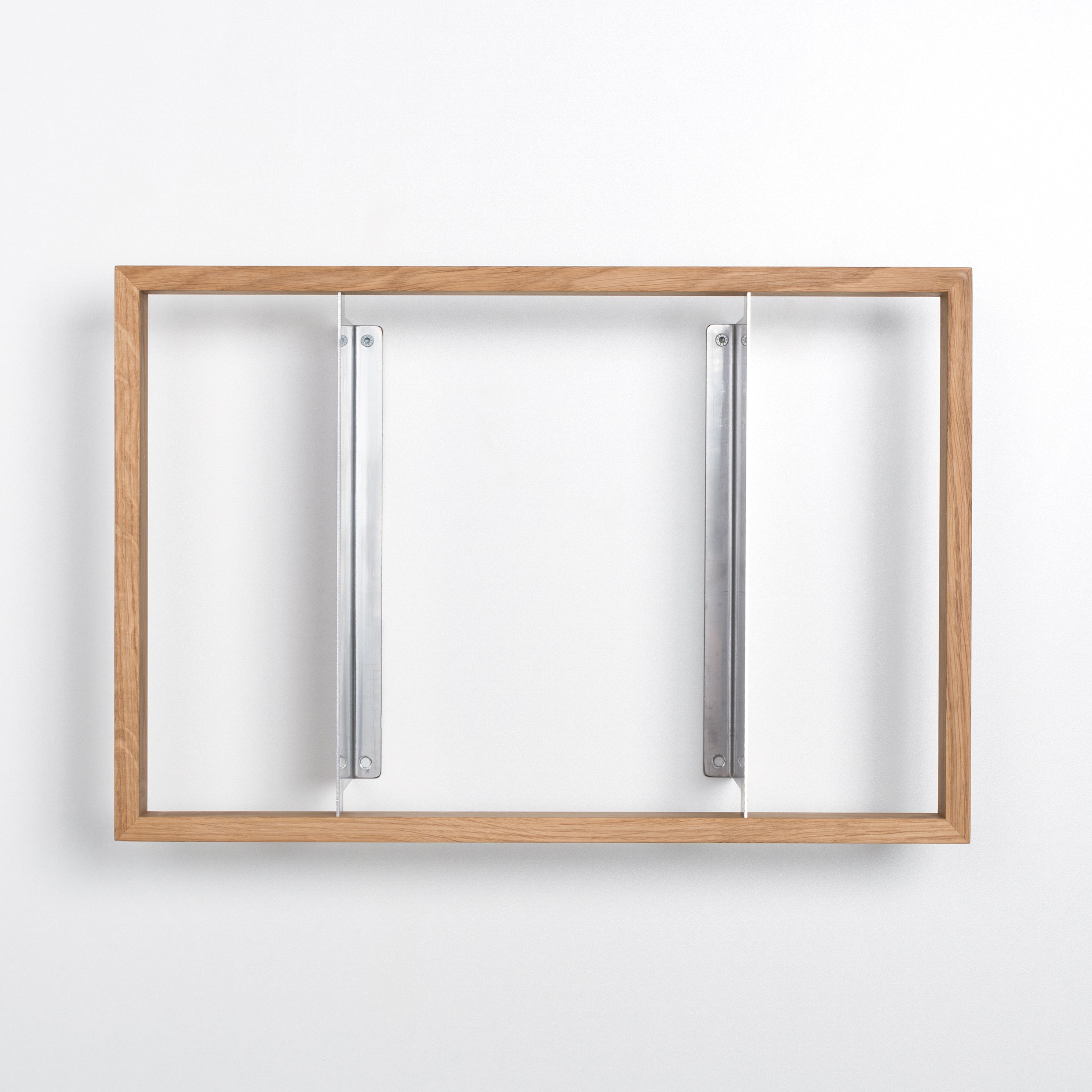 The b 12.2 by Das kleine b features a wooden rectangular frame with stainless steel angles and two vertical metal brackets, elegantly mounted on a blank white wall.