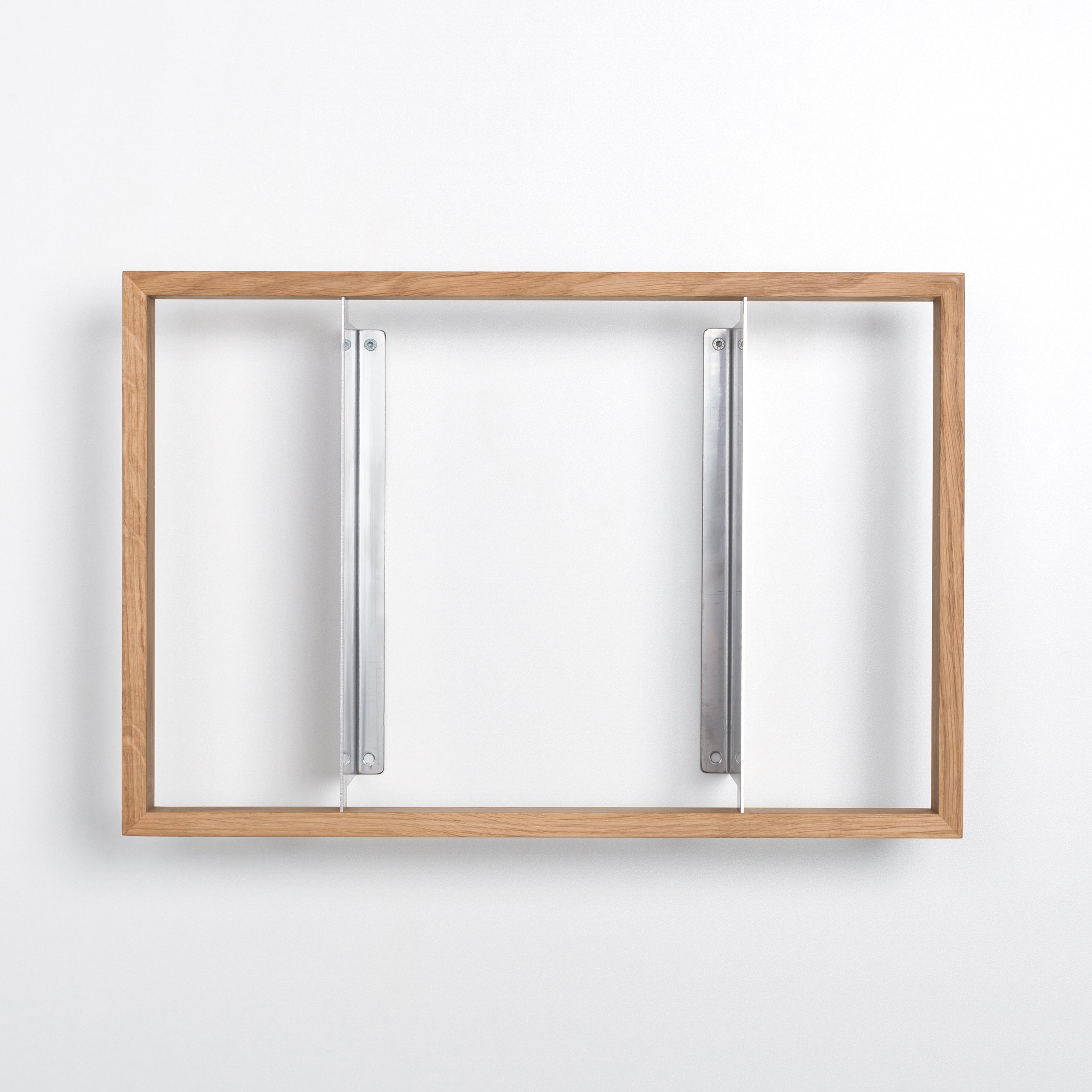 The b 8.7 wooden picture frame by Das kleine b features discreet stainless steel angles, mounted on a white wall.