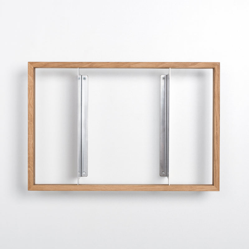 The b 8.7 wooden picture frame by Das kleine b features discreet stainless steel angles, mounted on a white wall.