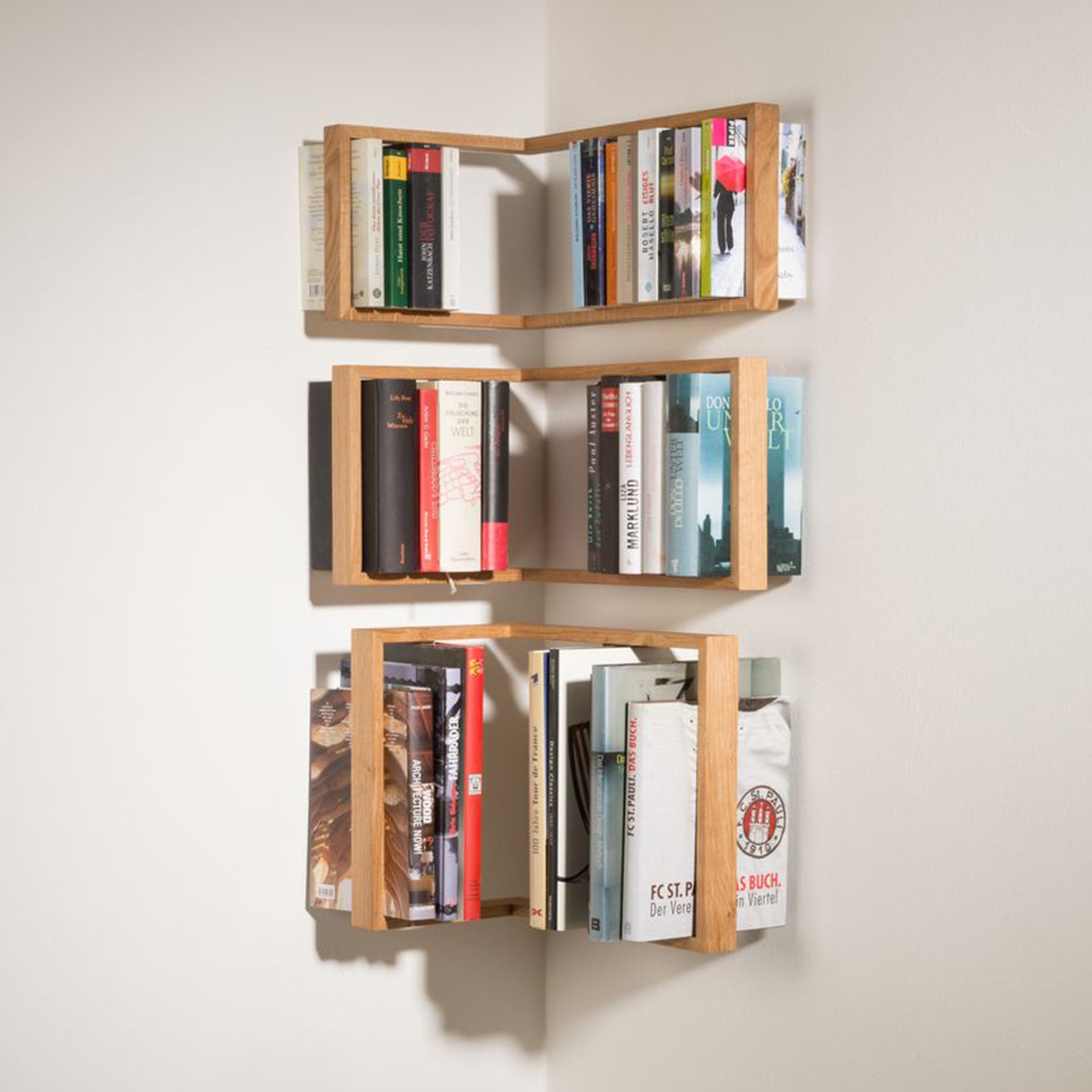 The b corner - Sale by Das kleine b is a solid wooden, minimalist floating wall-mounted corner bookshelf. It features three vertical tiers to showcase books, efficiently uses corner space, and enhances room aesthetics with its light wood design that blends style with functionality.