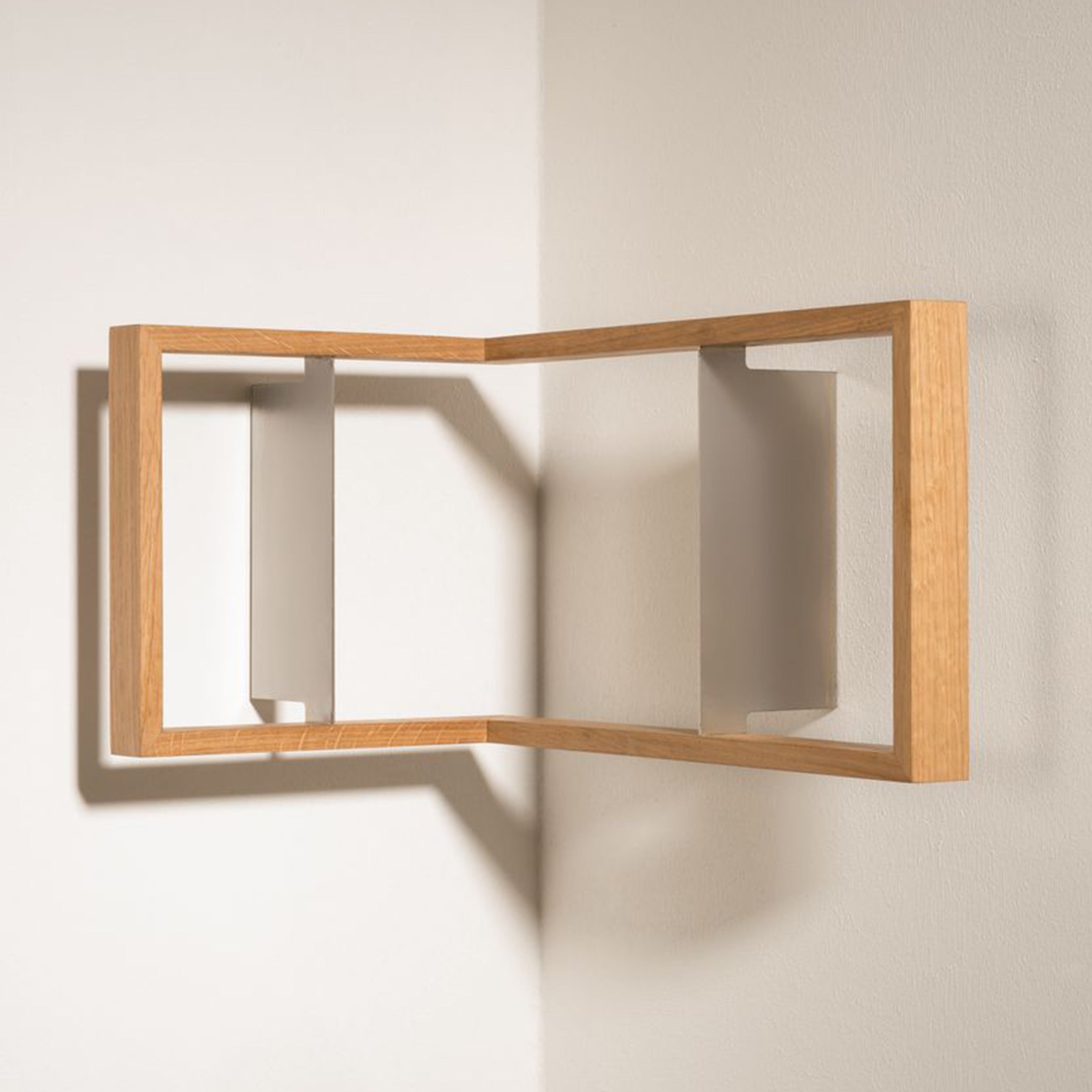 The b corner by Das kleine b is a wooden shelf that resembles an open book floating on a light wall. Its angular design and solid frame craft a clever visual illusion, blending modern and minimalist styles effortlessly.