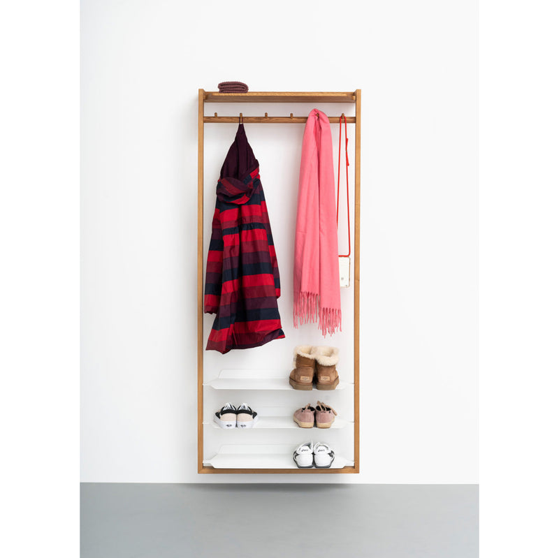 The Gardero-b by Das kleine b, an oiled oak wall-mounted coat rack featuring a wooden frame, gracefully holds a striped red and black jacket and pink scarf. Below are three shelves for shoes: brown boots, beige shoes, and white sneakers, with a small basket above this elegant corridor piece.