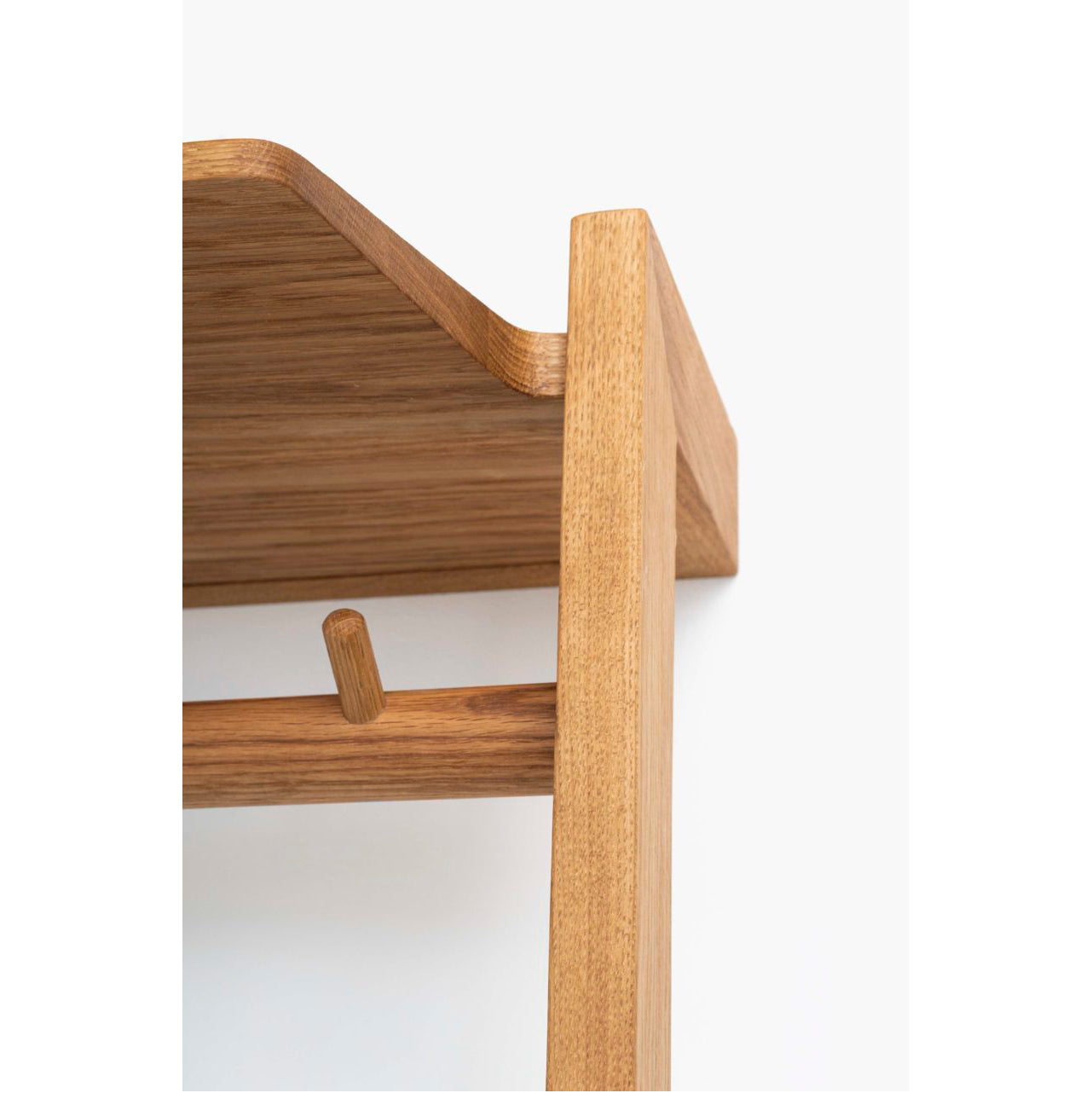 A close-up shows the Das kleine b Gardero-b with Hook Rail, featuring a minimalistic wooden shelf crafted from oiled oak. Its light brown finish, rounded peg, and corner junction are highlighted against a plain white background, perfect as corridor furniture.