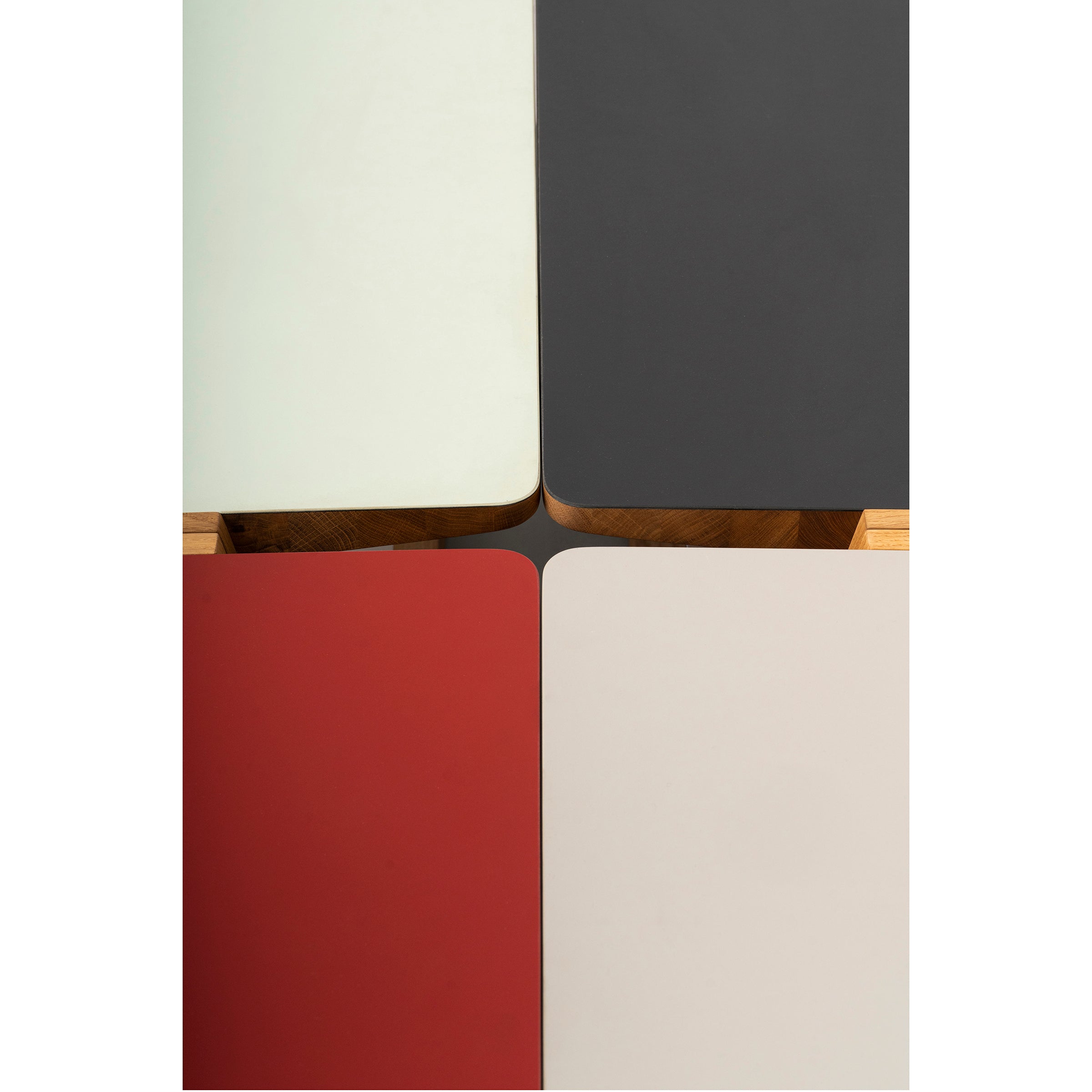 Four Bench Bänkle tables by Das kleine b, with black, white, red, and light green tabletops are arranged in a square. Their wooden legs meet centrally for a sleek minimalist geometric design perfect for saving space.