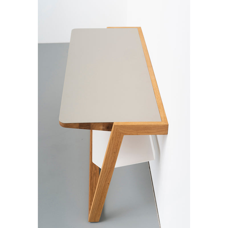 The Bench Bänkle from Das kleine b features a minimalist design with a light gray surface and angular wooden legs. Its sleek, contemporary geometric frame complements space-saving furniture, creating an uncluttered look against a white and gray wall background.