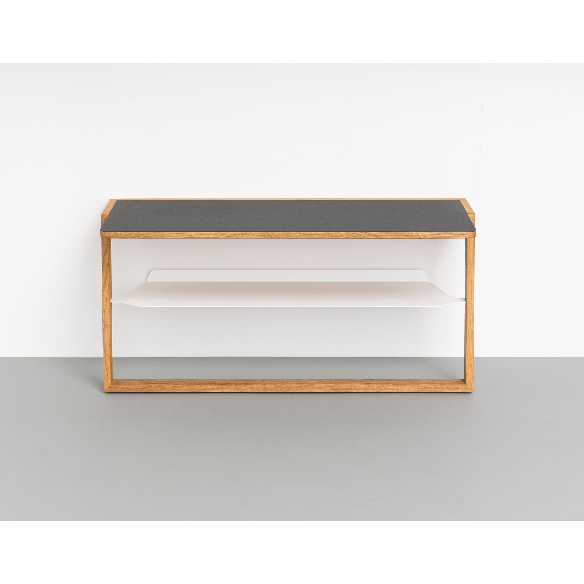 The Bench Bänkle by Das kleine b is a minimalist wall-mounted shelf featuring a wooden structure with an aluminum top and white interior. It offers two horizontal compartments, ideal for space-saving against a light gray wall and floor backdrop.