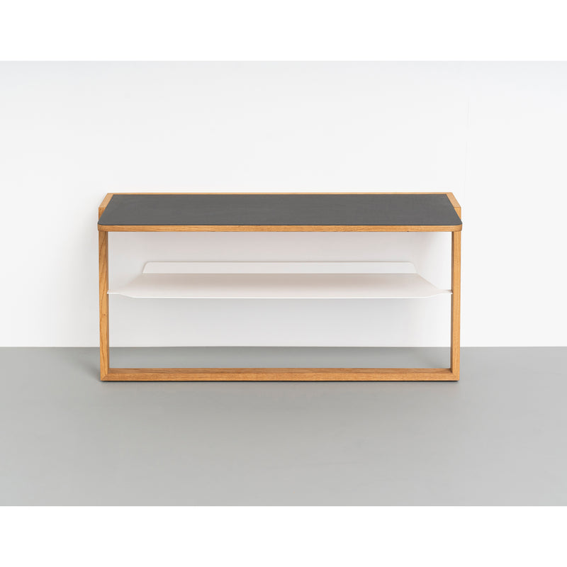 The Bench Bänkle by Das kleine b is a minimalist wall-mounted shelf featuring a wooden structure with an aluminum top and white interior. It offers two horizontal compartments, ideal for space-saving against a light gray wall and floor backdrop.
