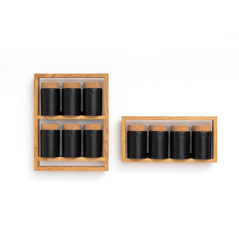 Two Das kleine b Spice Rack Bocuse units, crafted from oak, stand against a white background. The left rack holds six black spice jars with cork lids, and the right rack holds four similar jars. Each jar is perfectly aligned within the racks.