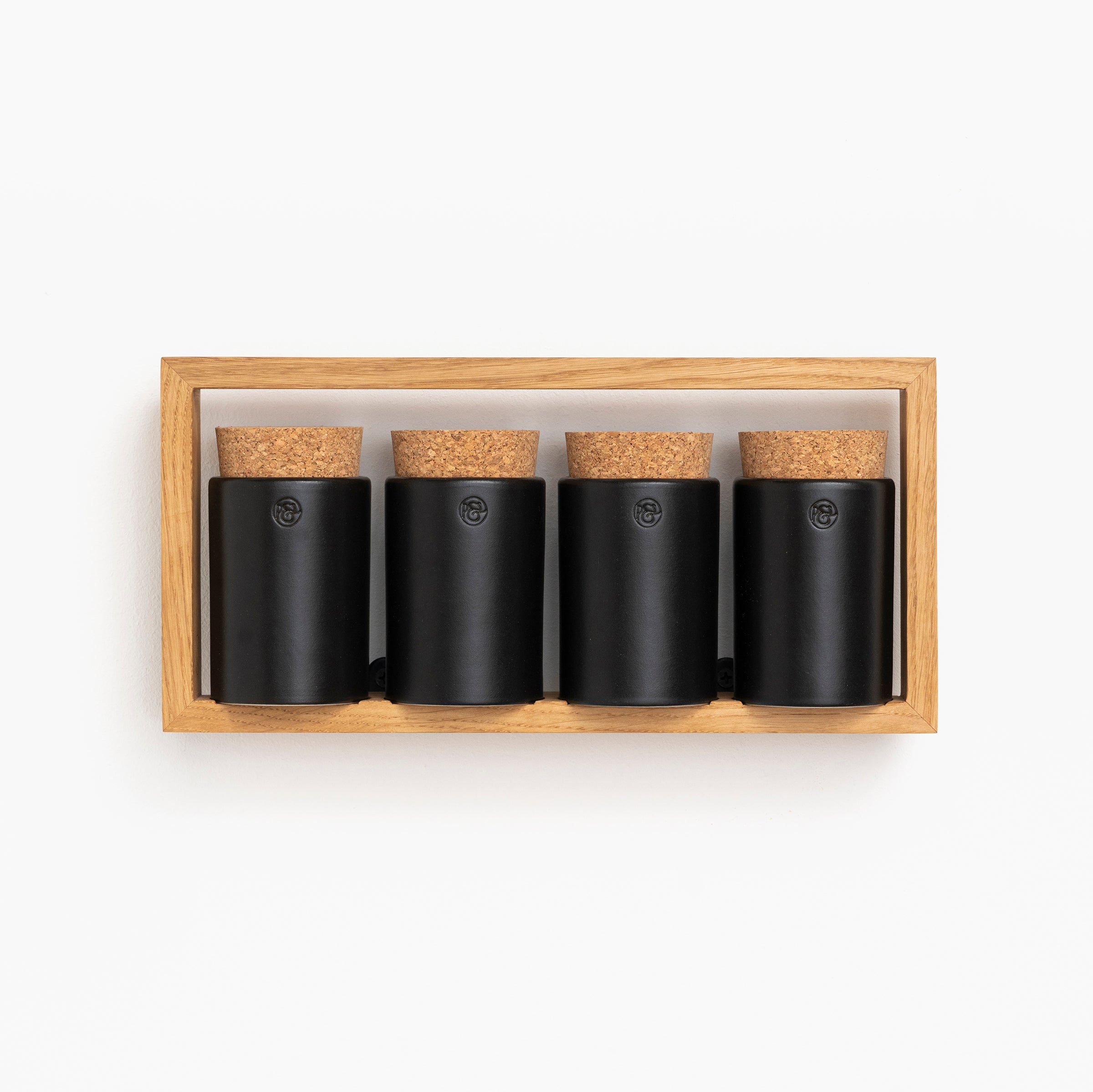 The Spice Rack Bocuse from Das kleine b features four sleek black cylindrical spice jars with cork lids, neatly arranged in an oak tray against a pristine white background.