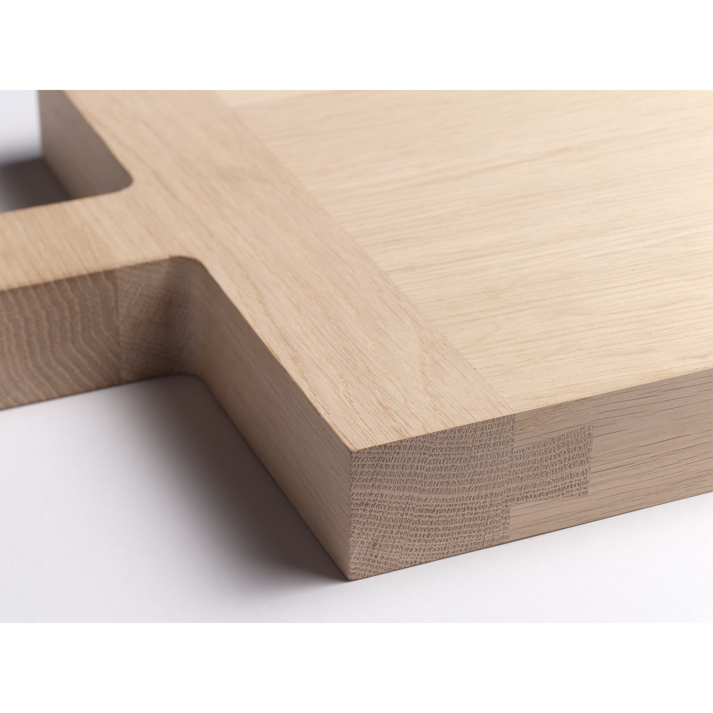 A close-up of the E15 AC06 CHOP wooden chopping board with a rectangular handle highlights intricate dovetail details at the corner, showcasing the grain and craftsmanship of European oak. The smooth, well-finished surface is evident.