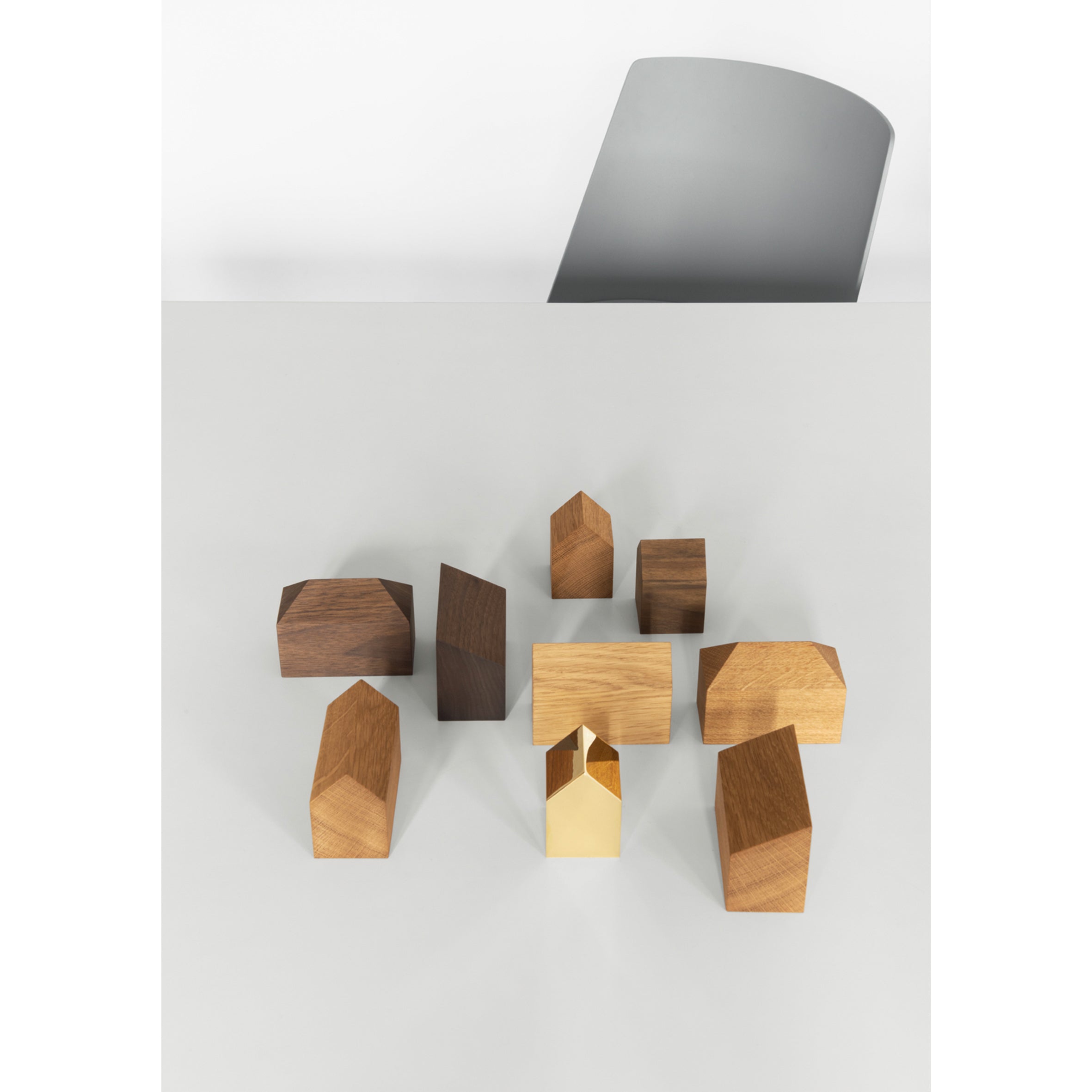 European oak wooden blocks shaped like small houses, with one gold block, are set on a light tabletop. This artistic desk accessory and unique AC10 HAUS paperweight by E15 has part of a gray chair in the background.