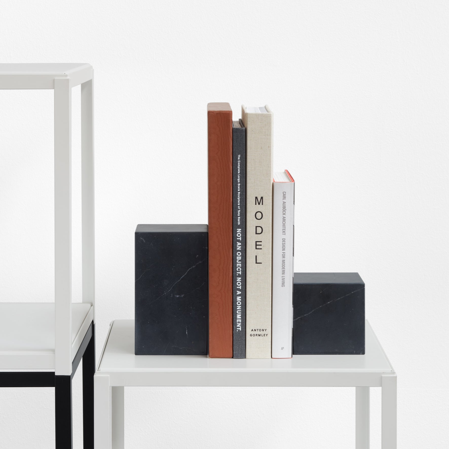 Four books rest elegantly between two black marble AC11 STOP bookends by E15 on a sleek, minimalistic shelf, exuding simplicity and modernity in a Philipp Mainzer design against a clean white background.