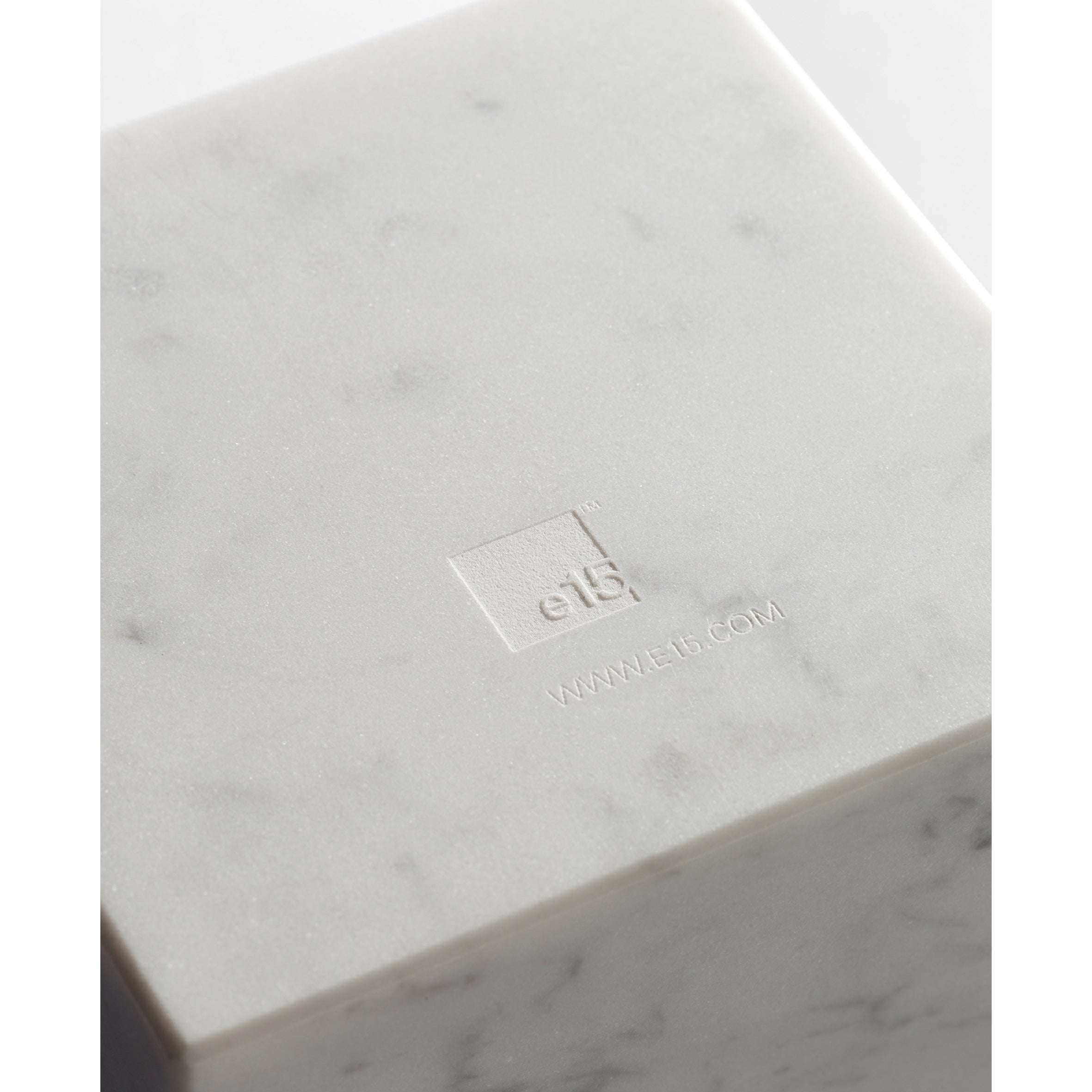 Close-up of the white marble-textured AC11 STOP cube from E15, showcasing its embossed logo and website. With a minimalist design by Philipp Mainzer, its subtly veined marble surface evokes sophistication reminiscent of a refined bookend.