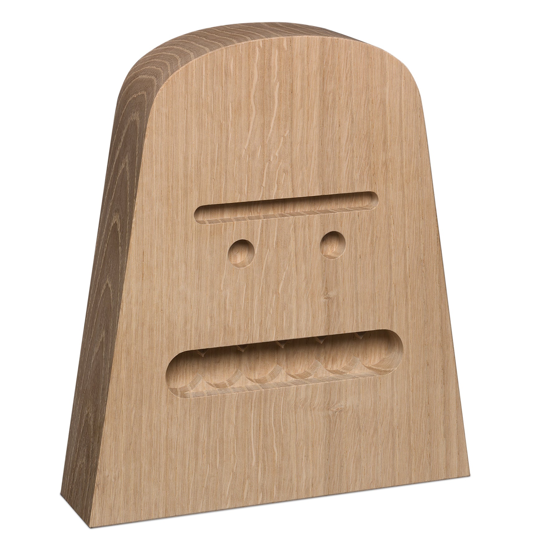 The AC17 BIG B by E15 is a wooden sculpture shaped like a rounded triangle, featuring a carved face with circular eyes, straight-line eyebrows, and a large rectangular mouth. Made from untreated oak, the wood grain enhances the depth of this solid wood piece.
