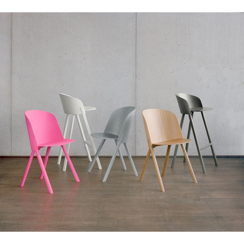Introducing the E15 CH05 THIS Side Chair series: a modern set of five chairs on a wooden floor against a concrete wall, each with unique finishes—pink, white, light gray, beige wood, and dark gray—crafted from sleek oak veneer plywood.