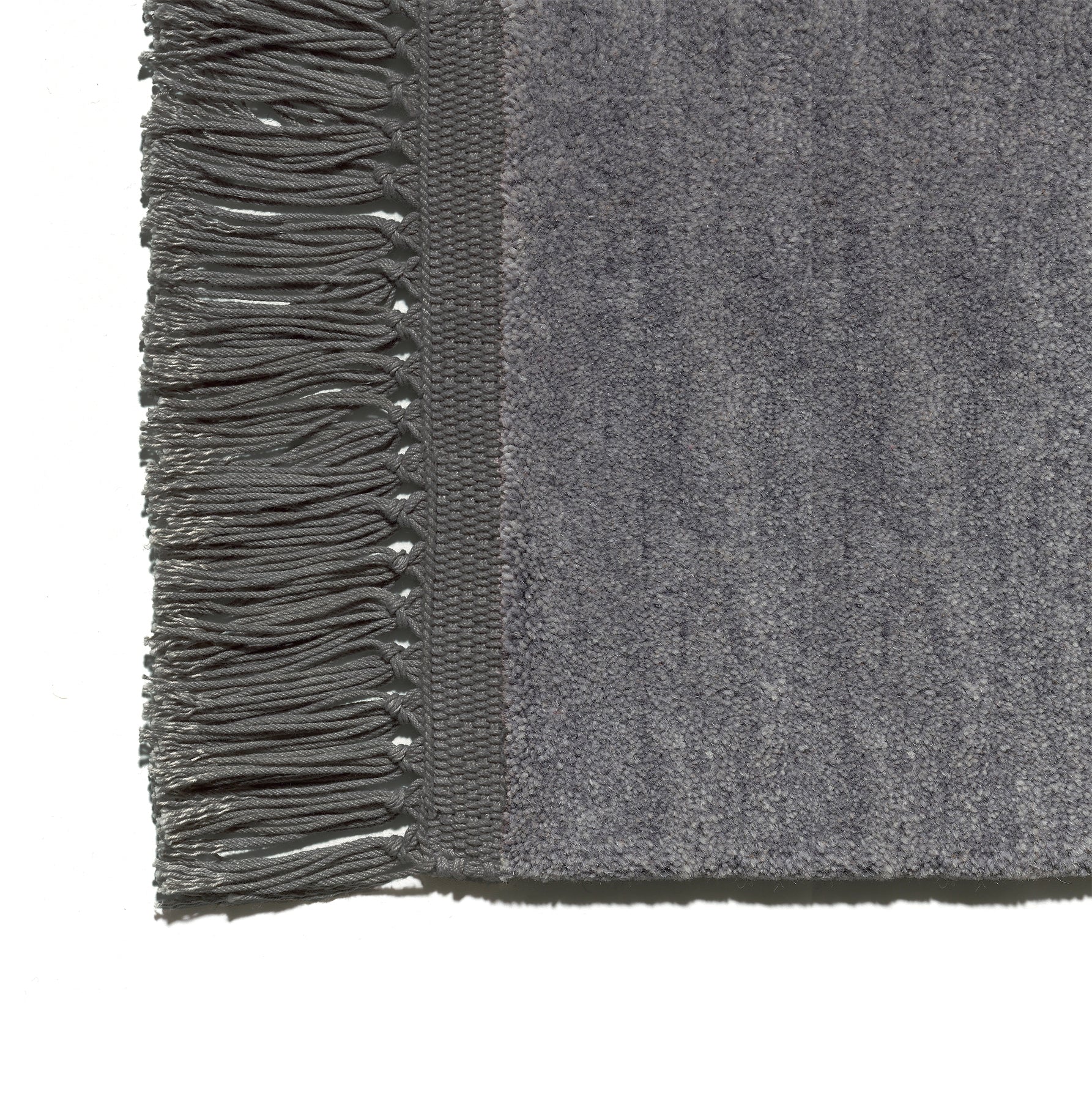 Close-up of the CP03 KAVIR by E15, a gray hand-woven carpet with textured fabric and fringed edges.