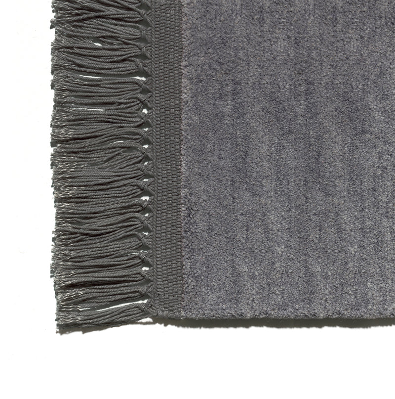 Close-up of the CP03 KAVIR by E15, a gray hand-woven carpet with textured fabric and fringed edges.