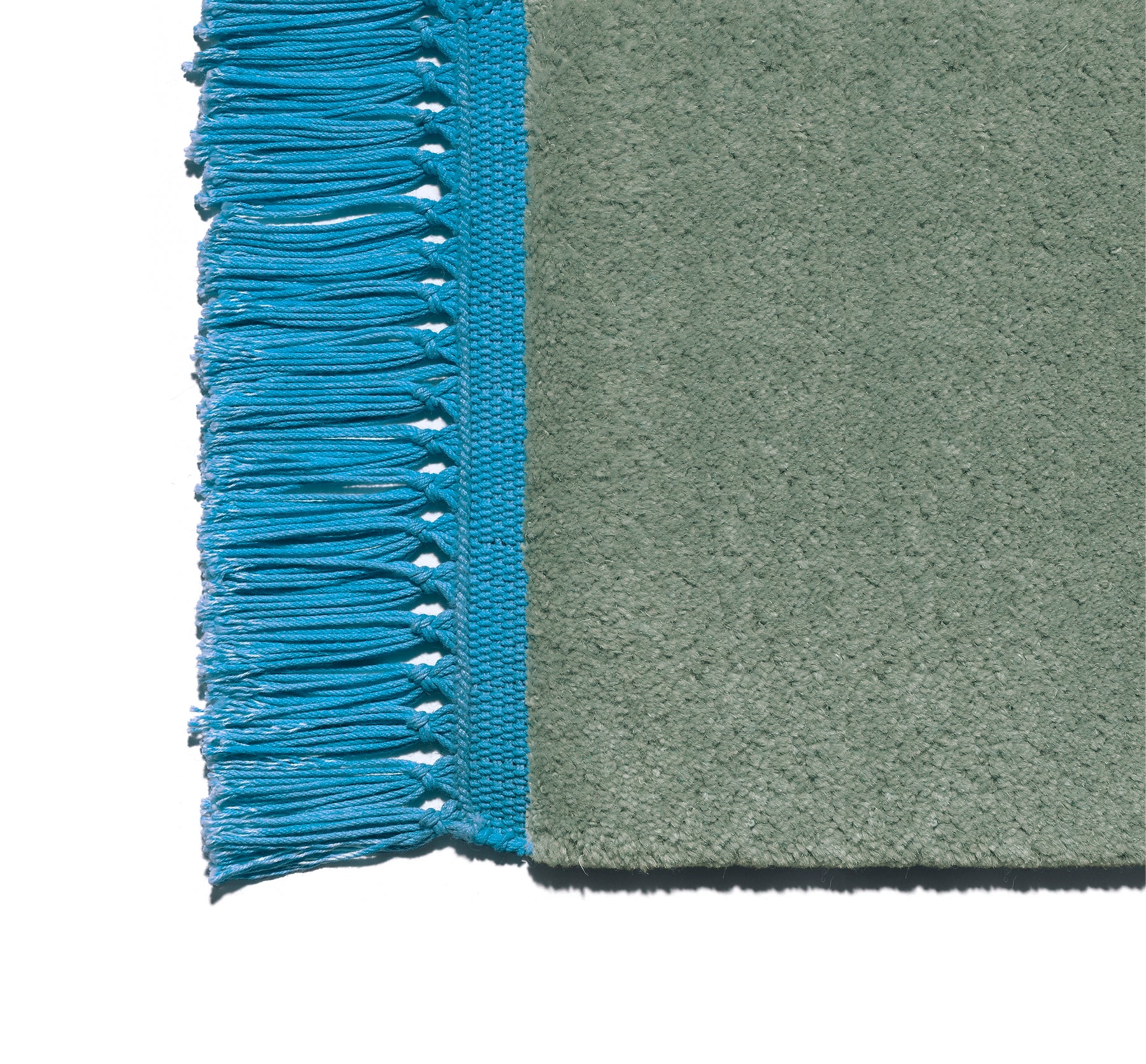 Close-up of E15s CP03 KAVIR carpet corner shows teal fringe on the left, textured green on the right. Its neatly woven border contrasts with smooth fabric, showcasing bright, vivid colors.
