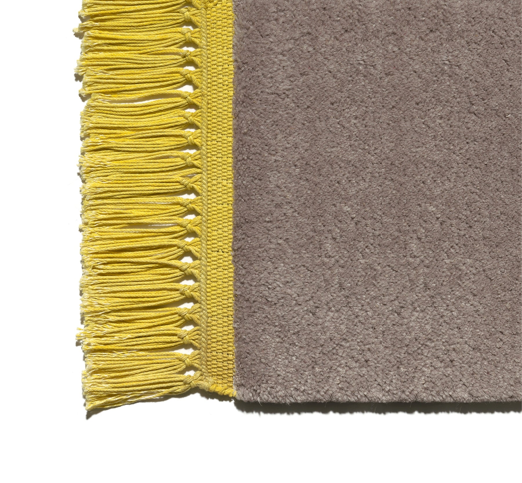 Close-up of a corner of the CP03 KAVIR by E15, a beige, hand-woven carpet with neatly arranged long yellow fringes. Its texture is soft and plush.
