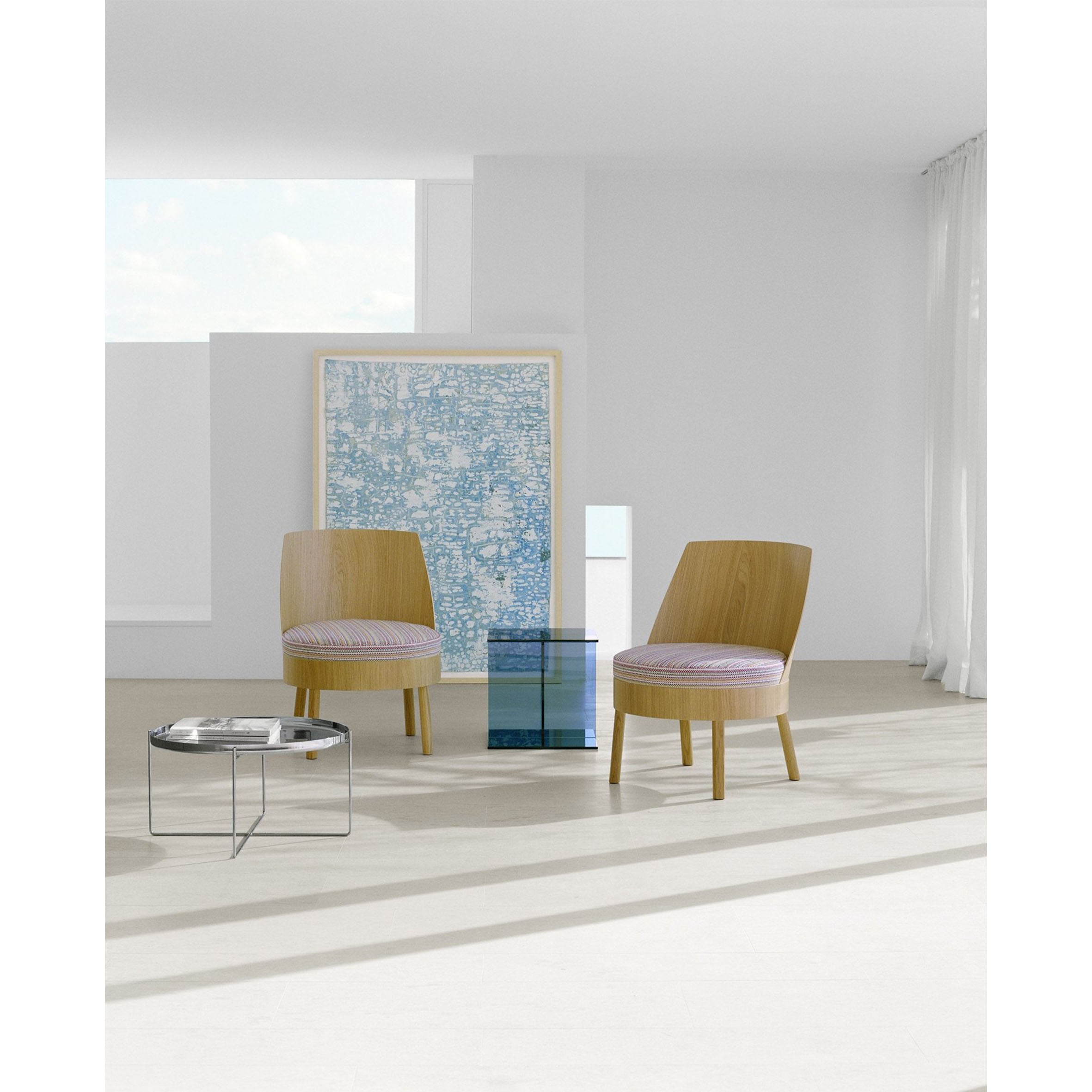 A minimalist room with two wooden chairs with striped cushions, a small wire-framed side table, and E15s CT08 VIER blue-tinted glass cube enhancing the large blue abstract artwork against a white wall. A sheer curtain softens light from the window.