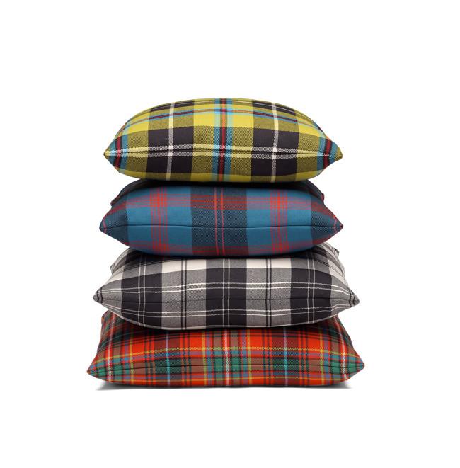 Four CU06 NIMA accessory cushions by E15, featuring colorful plaid patterns, are neatly stacked: yellow-green on top, blue next, black and white third, with vibrant orange at the base. These seating elements rest beautifully against a crisp white background.