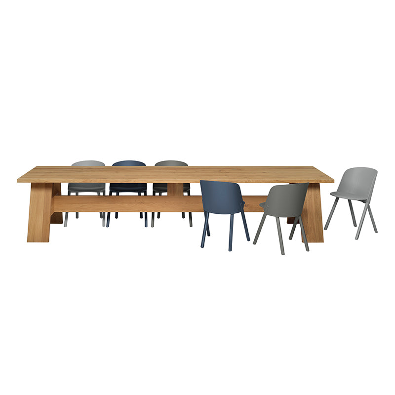 The DC01 FAYLAND, a long solid wood table by E15 with a natural finish, is encircled by seven chairs in gray and blue hues. Evoking David Chipperfields refined design, this elegant ensemble stands against a plain white backdrop.