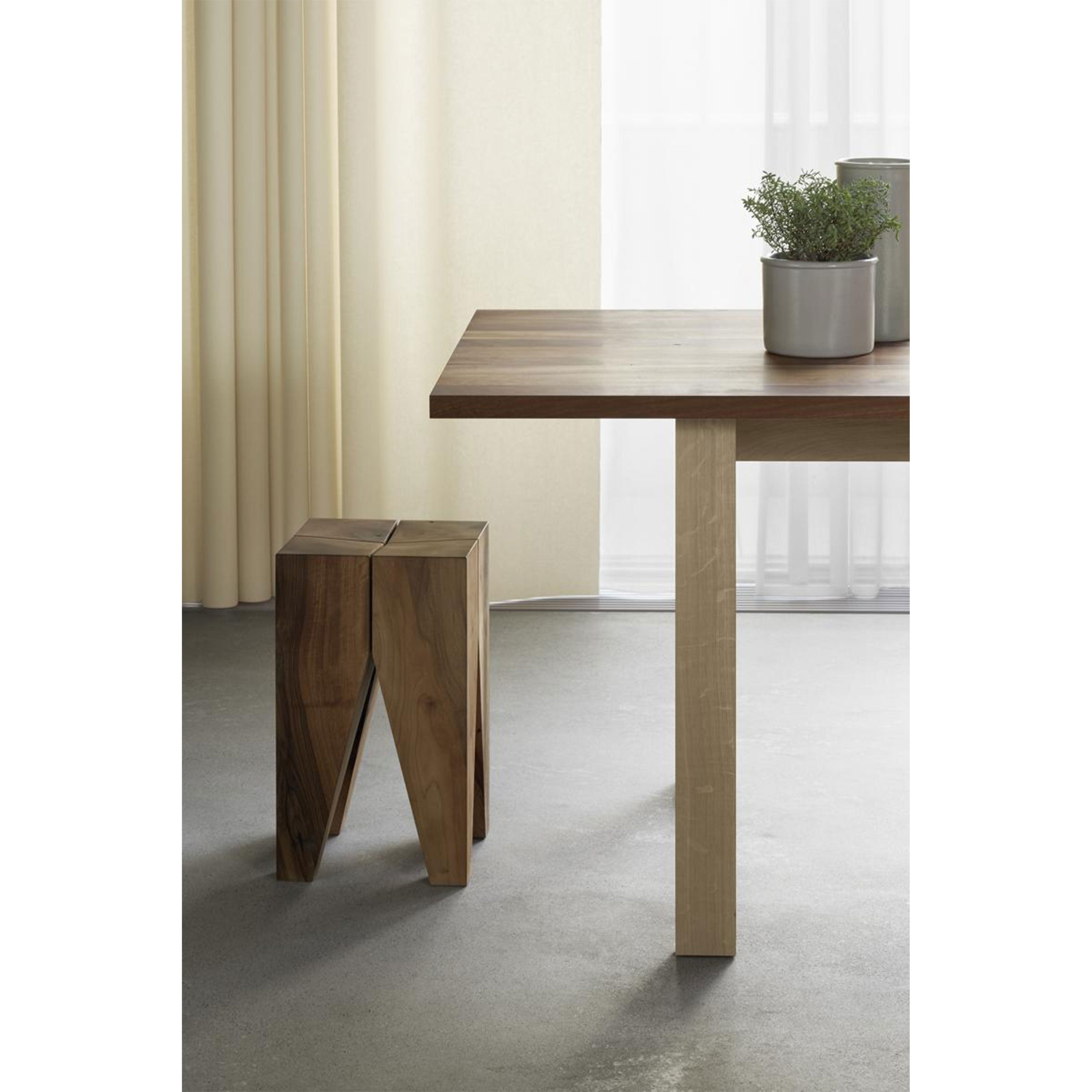 Minimalist interior with an E15 DC08 Basis Table and matching wooden stool. The table holds a potted plant, while sheer curtains let soft light filter in for serenity. Gray floor complements the natural wood tones, highlighting the solid wood trestles beautifully.