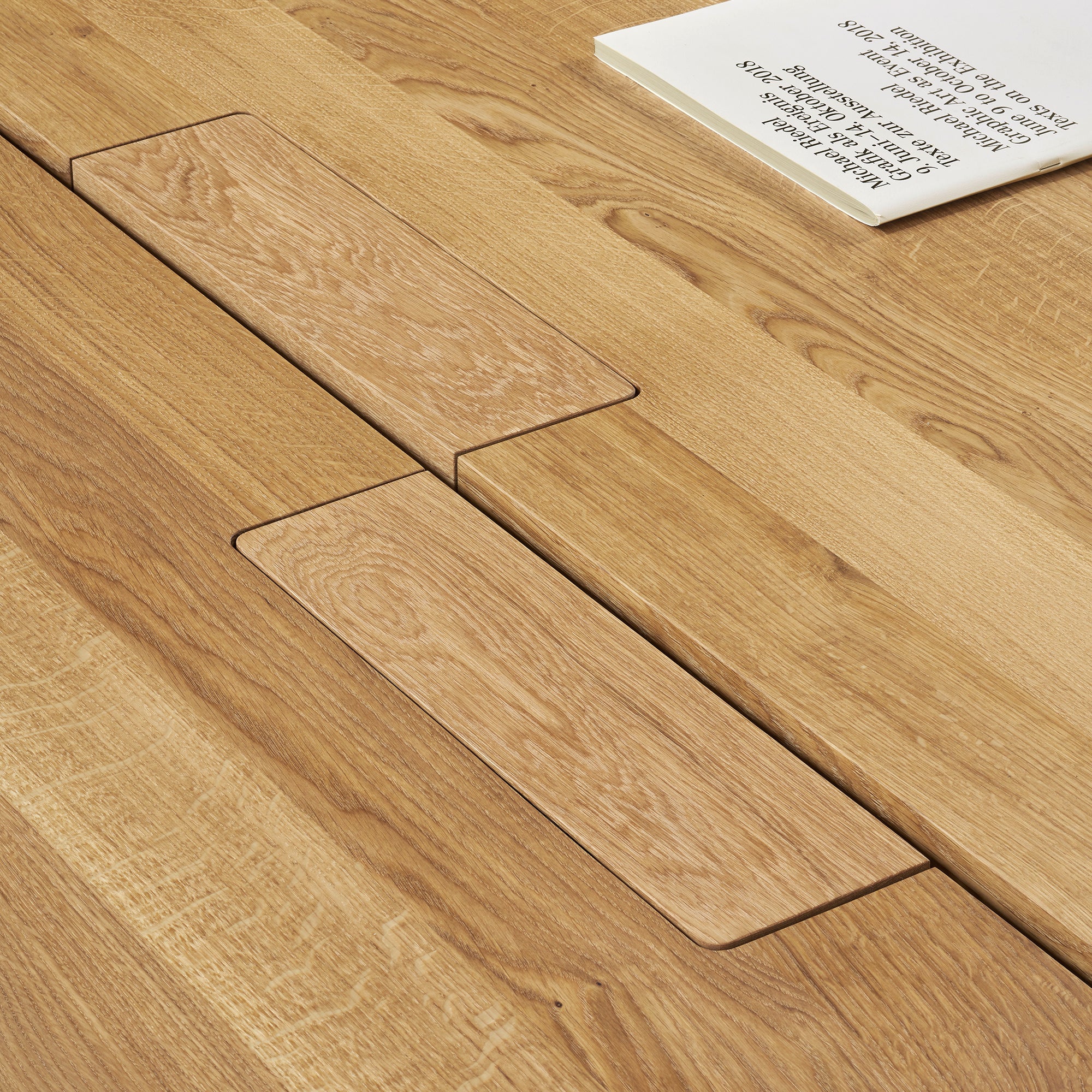 The DC08 Basis Workstation by E15 features a seamless wooden design with precise joinery. An open book with visible text rests on it, while the woodgrain offers a natural, textured look—ideal for creative workspaces.