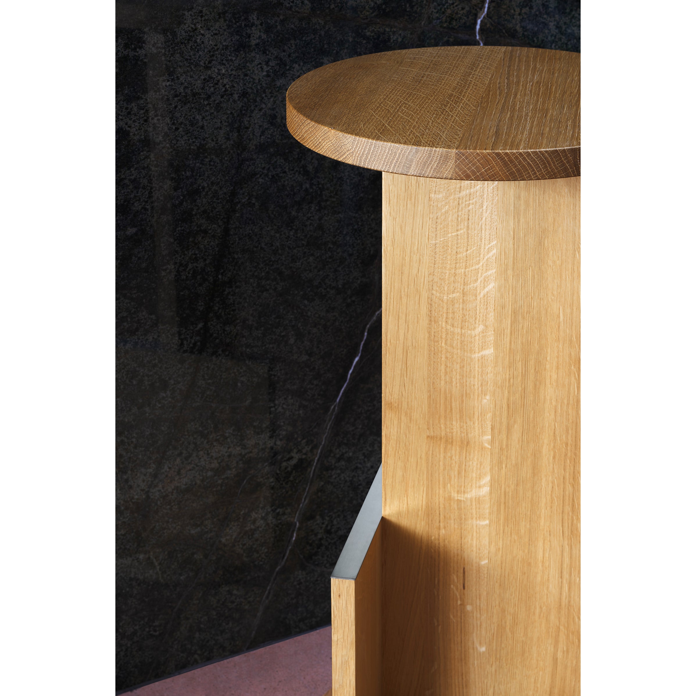 The DT01 Tank Barstool by E15, crafted from solid European oak, features a round top highlighting natural wood grain. Set against a dark marble-like backdrop, it sits gracefully on a light pink floor, evoking the elegance of David Thulstrups designs.