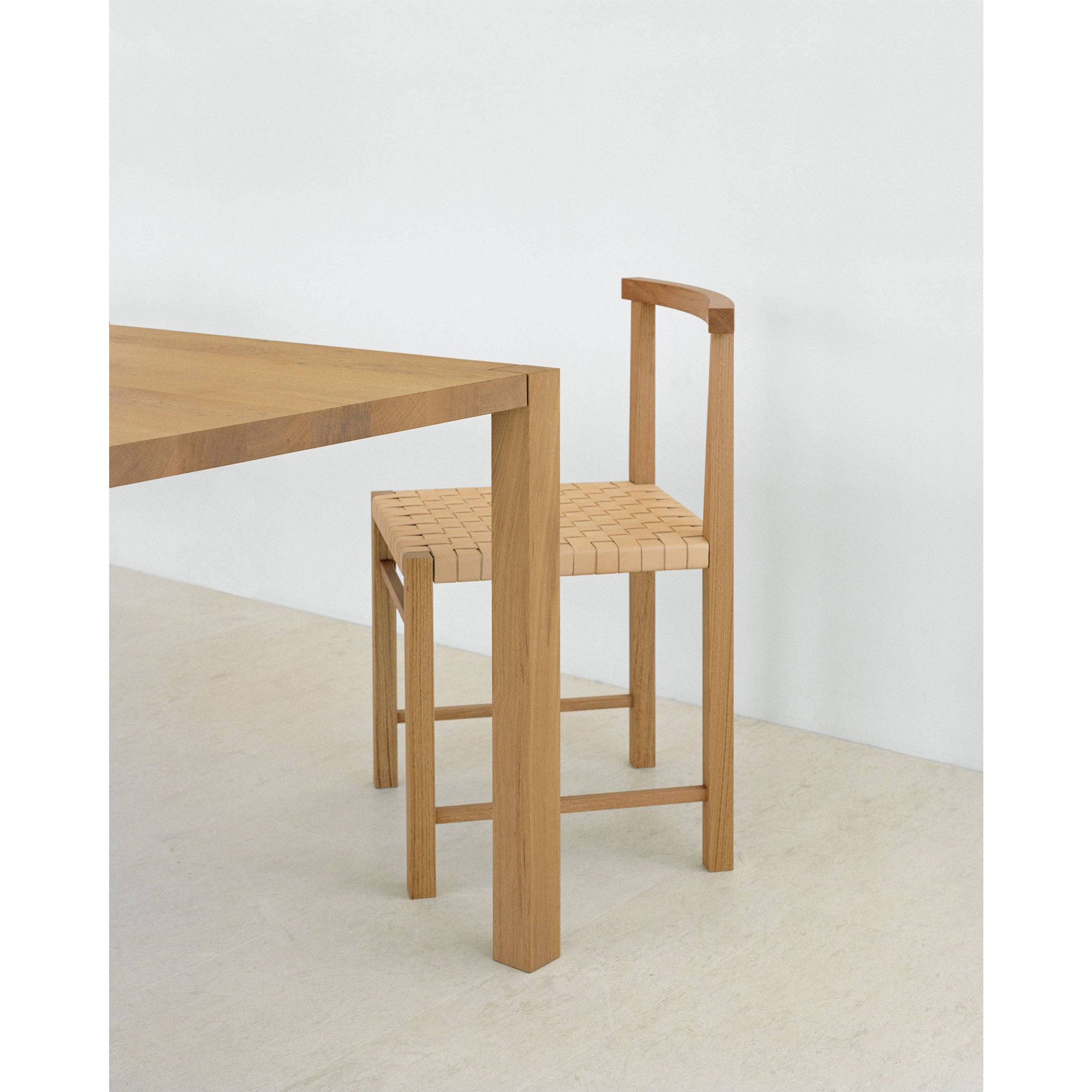 The E15 FK02 KARNAK chair by Ferdinand Kramer boasts a sleek waxed oak frame and woven seat, ideal alongside a wooden table in this bright, minimalist room with light floors and plain walls.