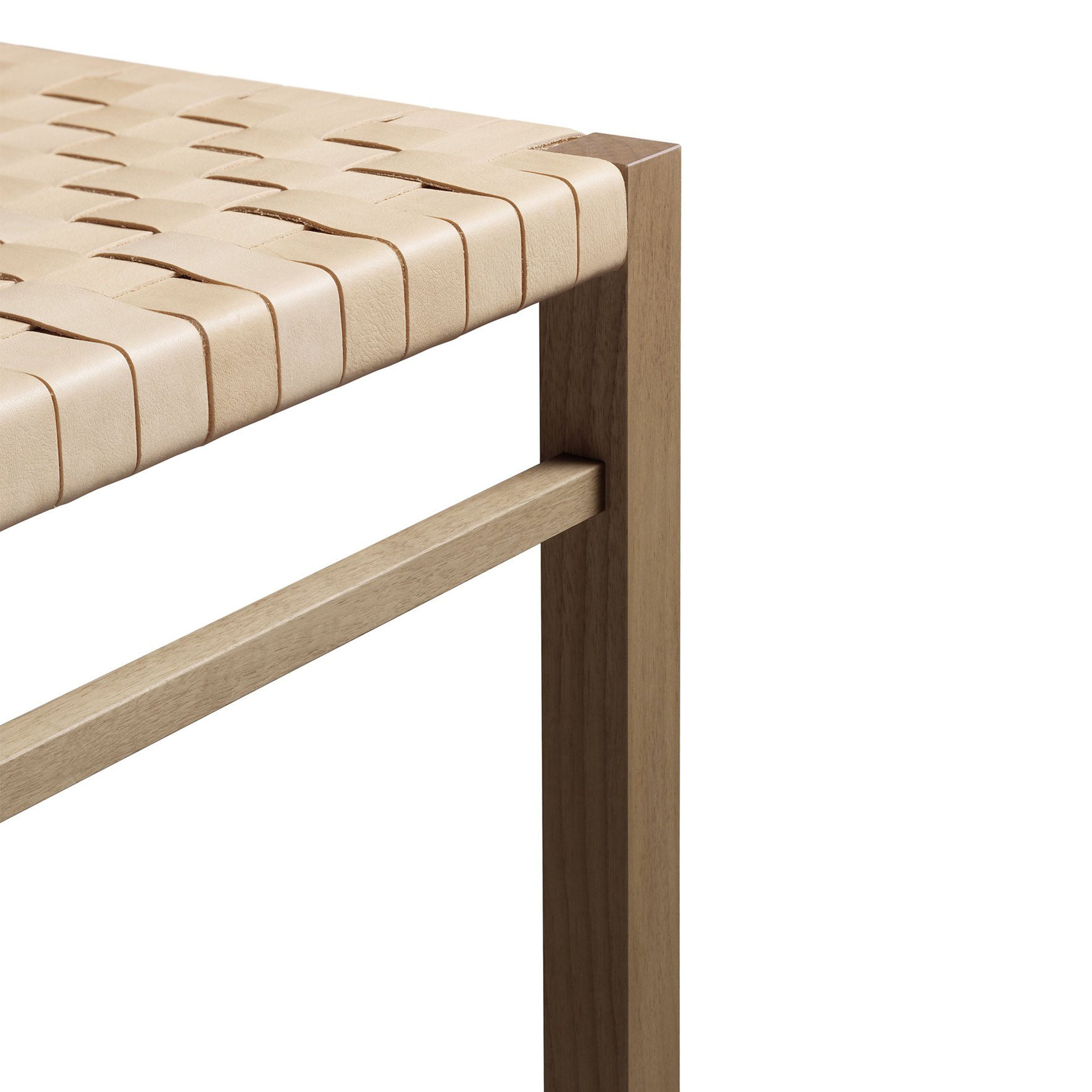 A close-up of a wooden bench corner highlights a handwoven beige leather seat on a minimalist waxed solid oak frame. This design, from E15, is reminiscent of the FK03 ASWAN with its clean lines and natural finish.