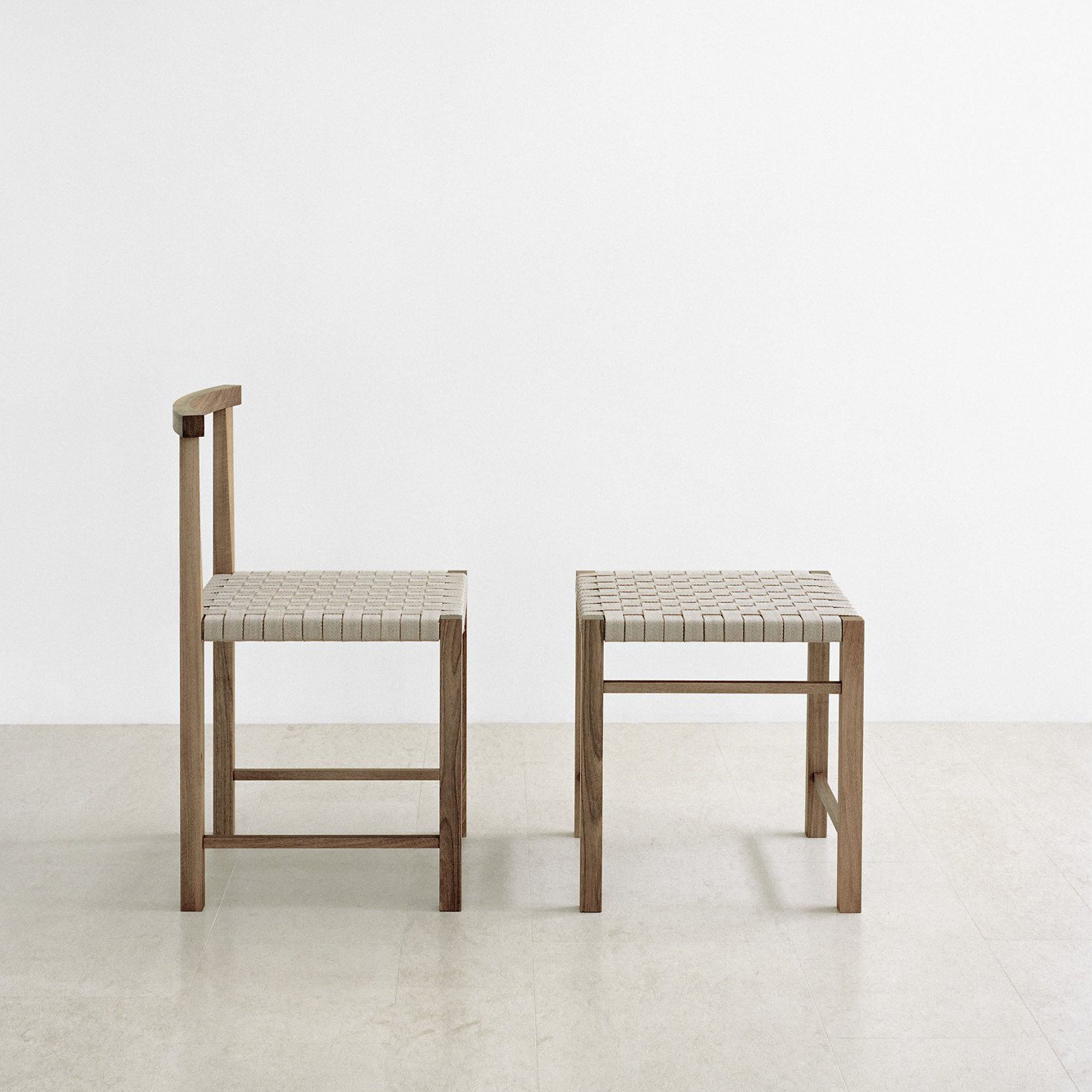 Two minimalist chairs with waxed solid oak frames and handwoven seats sit on a light-colored floor against a plain white background—one with a backrest and the other, E15’s FK03 ASWAN stool, highlighting its backless design.