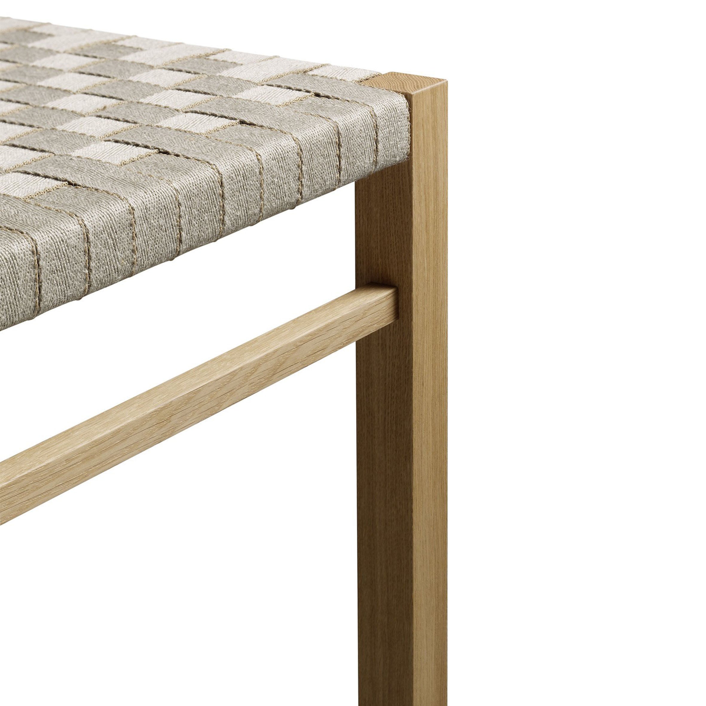 Close-up of the FK03 ASWAN wooden chair by E15, showcasing a minimalist design with legs and support bars in waxed solid oak, and a handwoven beige and gray fabric seat.