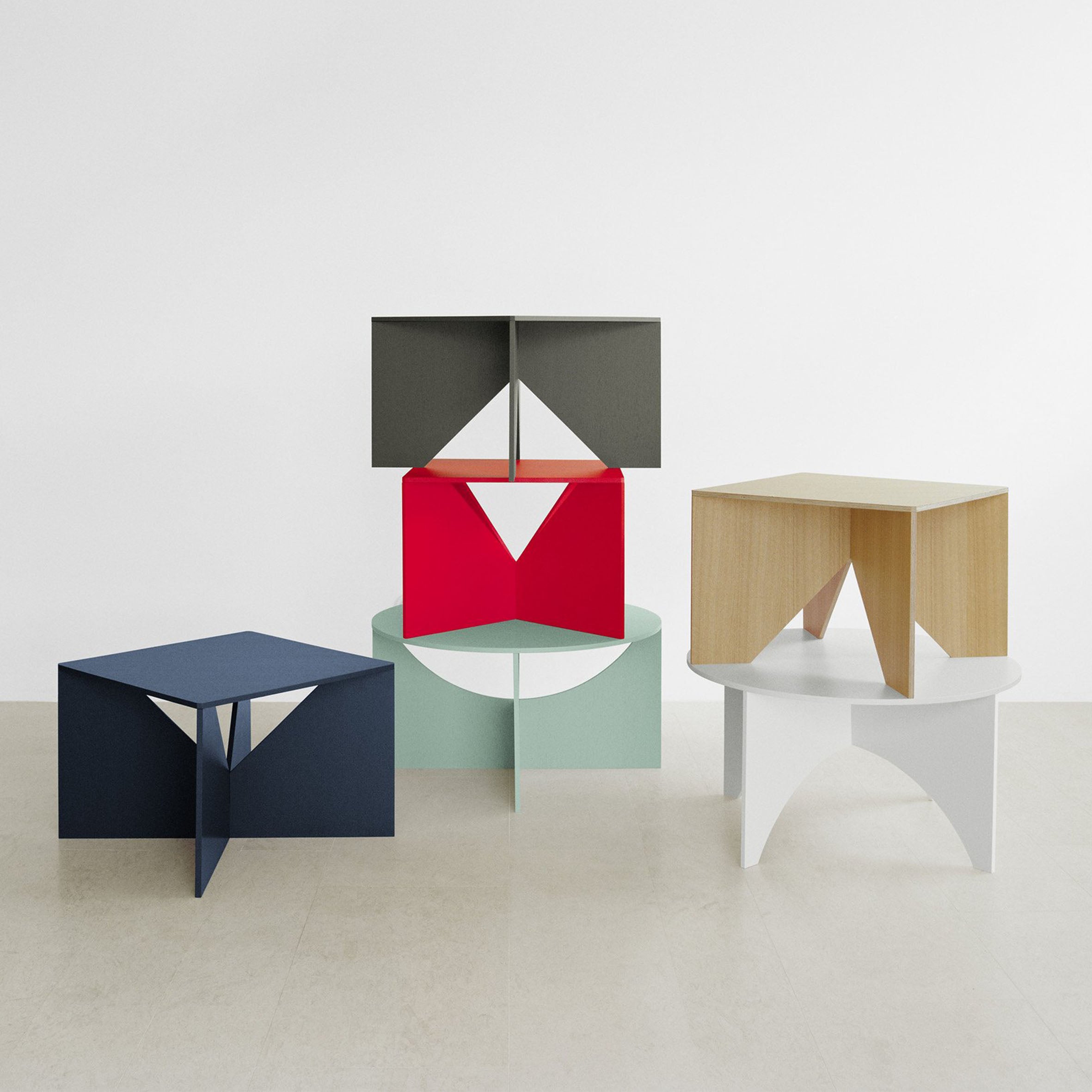 A set of modern geometric FK05 CHARLOTTE tables by E15, inspired by Ferdinand Kramer designs, featuring a green circle, red semi-circle, blue triangle, beige square, and dark gray rectangle are artistically displayed against a white background.