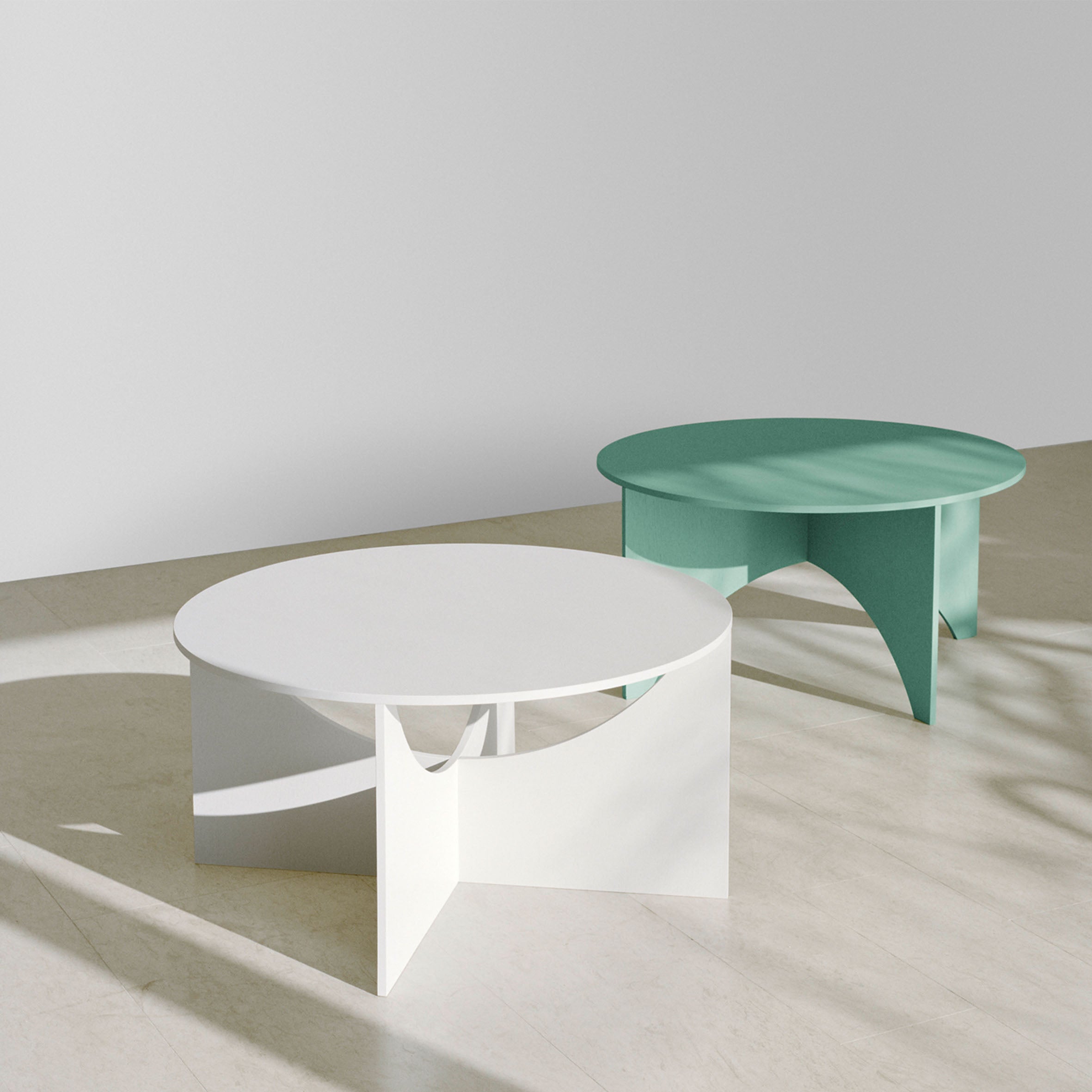 Two E15 FK05 CHARLOTTE coffee tables, one white and the other teal, with Ferdinand Kramers geometric base rest on a light floor. Sunlight dances across them, casting soft shadows against a plain wall.