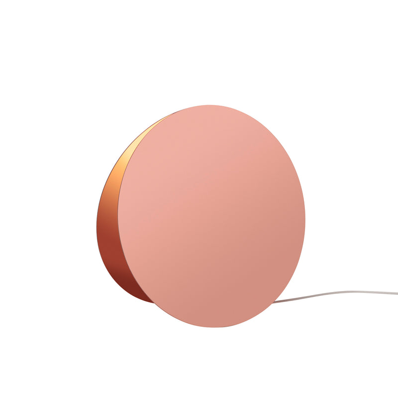 The LT05 NORTH Floor Light by E15 is a round, modern copper-colored lamp with a flat front. It features a minimalistic design, rests at a slight angle, and emits atmospheric light while connected to a white power cord.