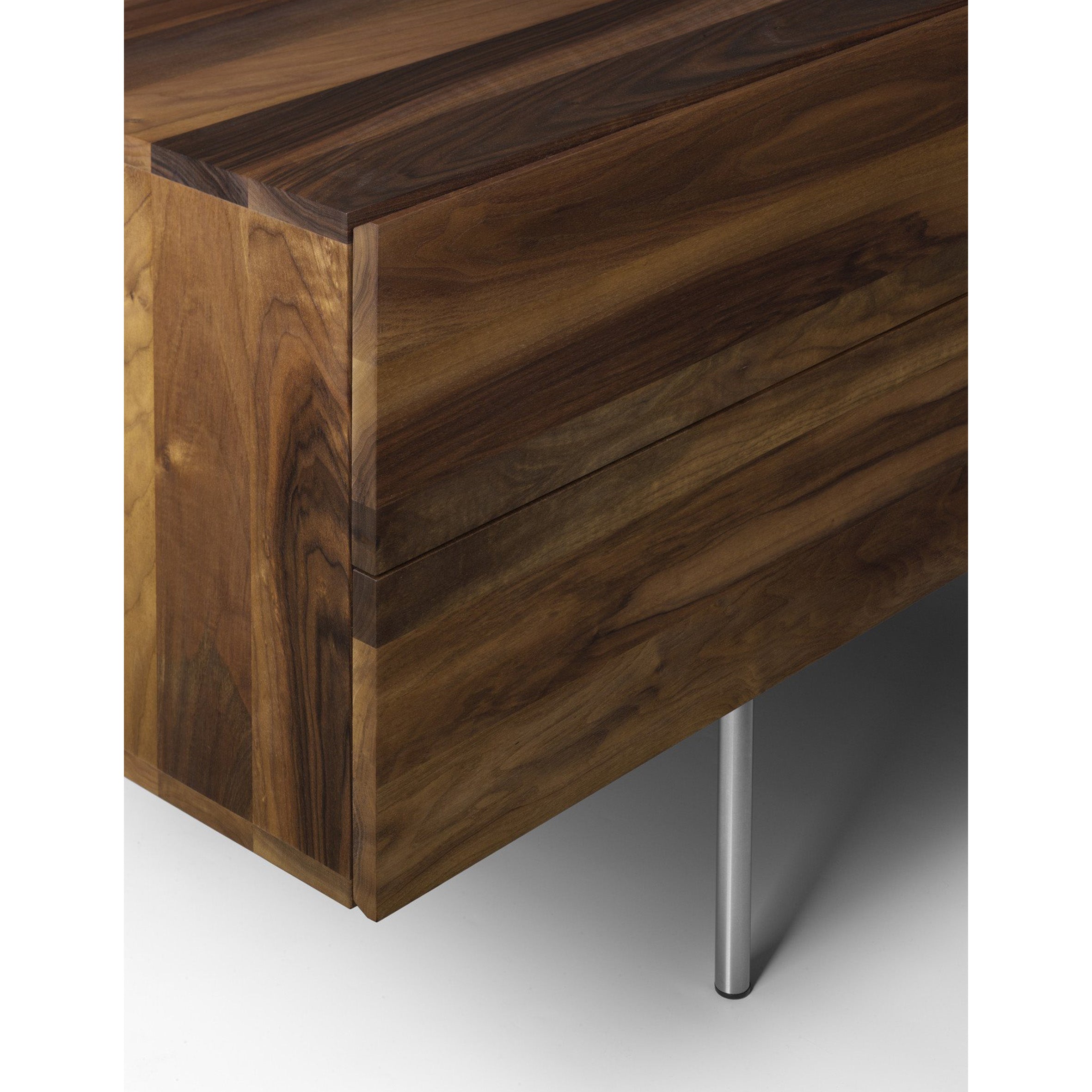 Close-up of the SB08 MAHNAZ by E15 showcases a modern wood table corner with a smooth, polished surface, distinct grain patterns, and chamfered edges. Its solid body is paired with sleek metal legs for a contemporary design.