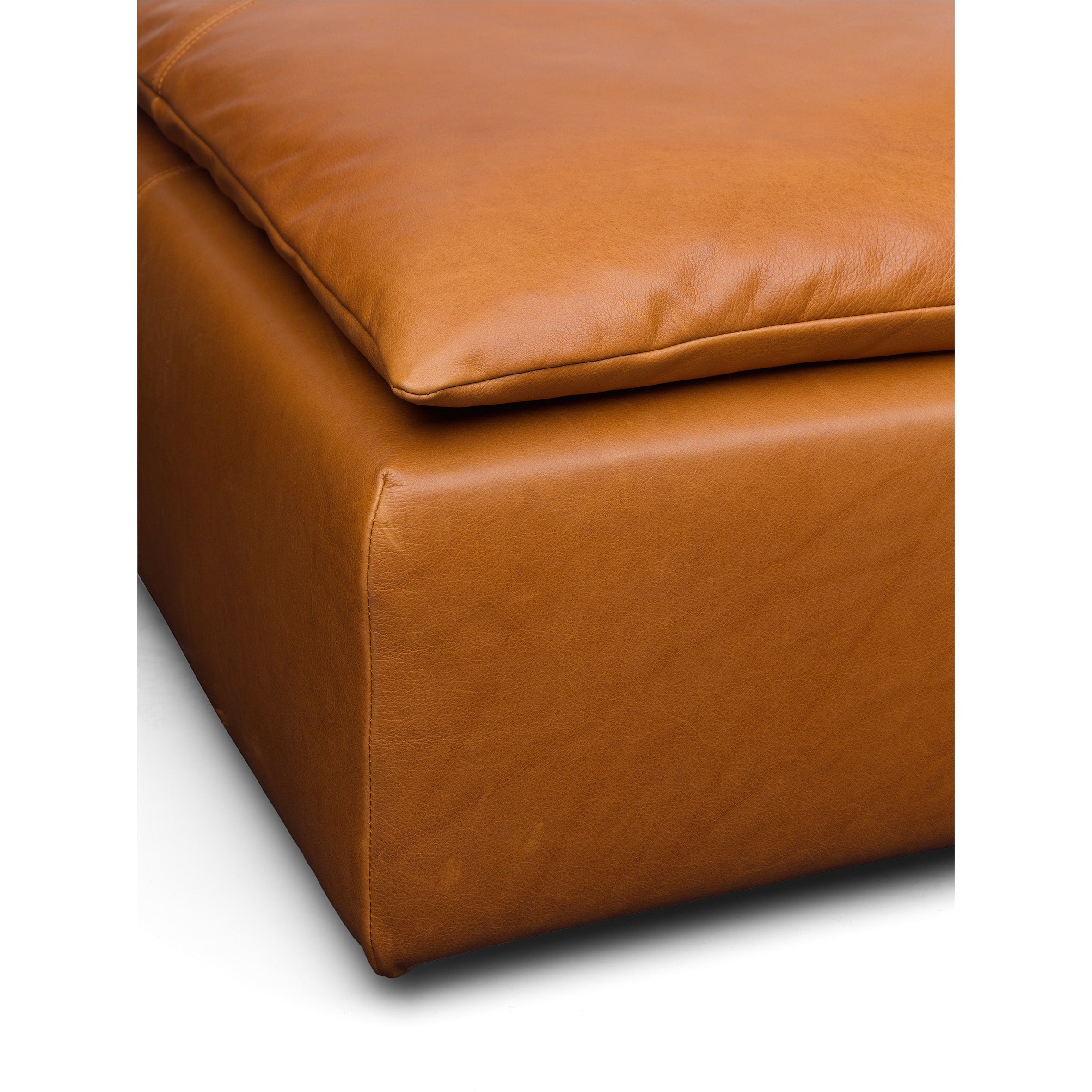 Close-up of an orange-brown leather SF03 SHIRAZ sofa cushion by E15, with visible stitching on top, resting on a matching base. The leathers smooth texture and subtle creases enhance the aesthetic against a white background.