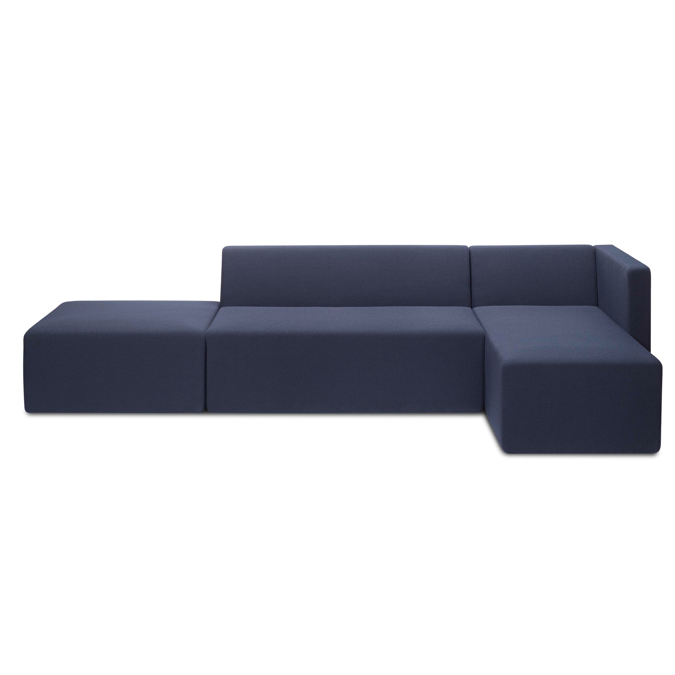 The SF06 KERMAN by E15 is a minimalist dark blue sectional sofa with L-shaped seating modules on a white backdrop. It features clean lines, a low profile, and a left-side chaise lounge, offering practicality with removable covers.