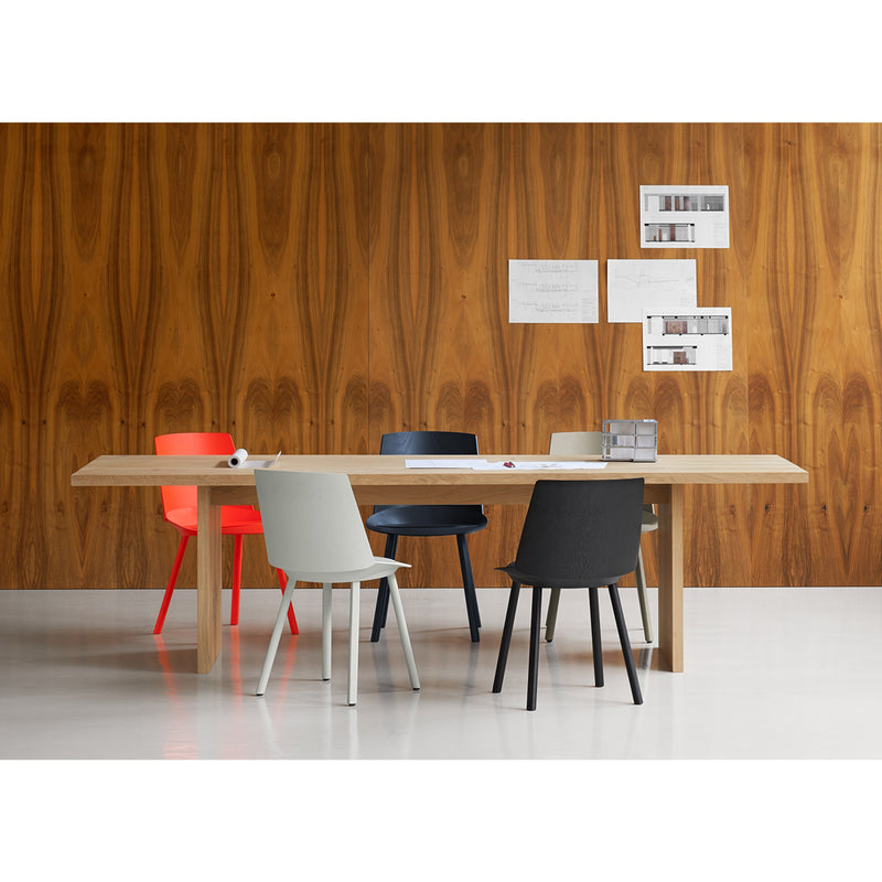The dining area features the E15 TA24 ASHIDA solid wood table, surrounded by chairs in red, beige, and black. The wall displays a natural grain pattern with three papers pinned to it. Crafted using Japanese techniques, the glossy white floor enhances the rooms elegance.